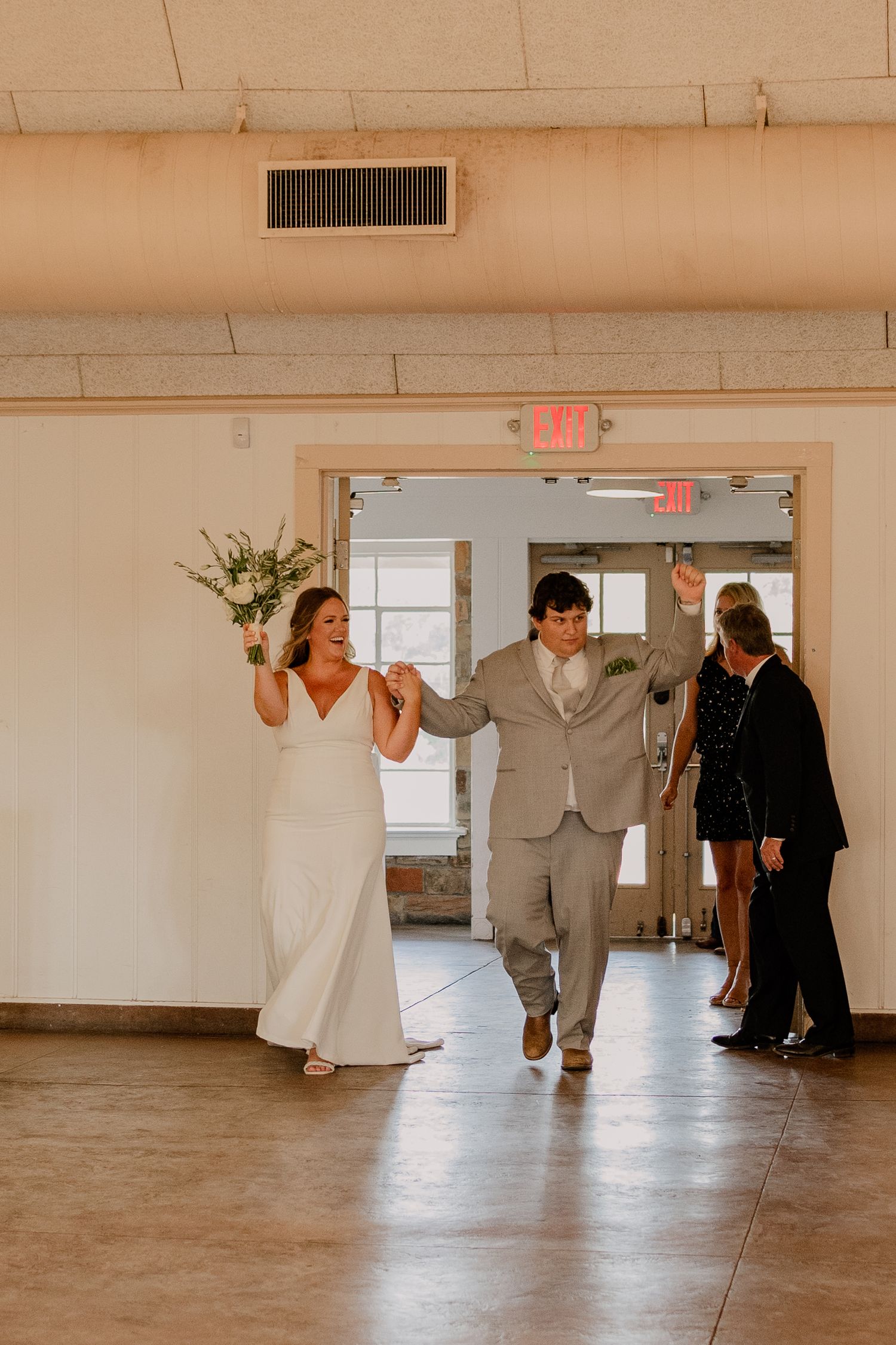 Bride and groom joyfully and candidly enter the bright East Dallas reception hall during their summer wedding