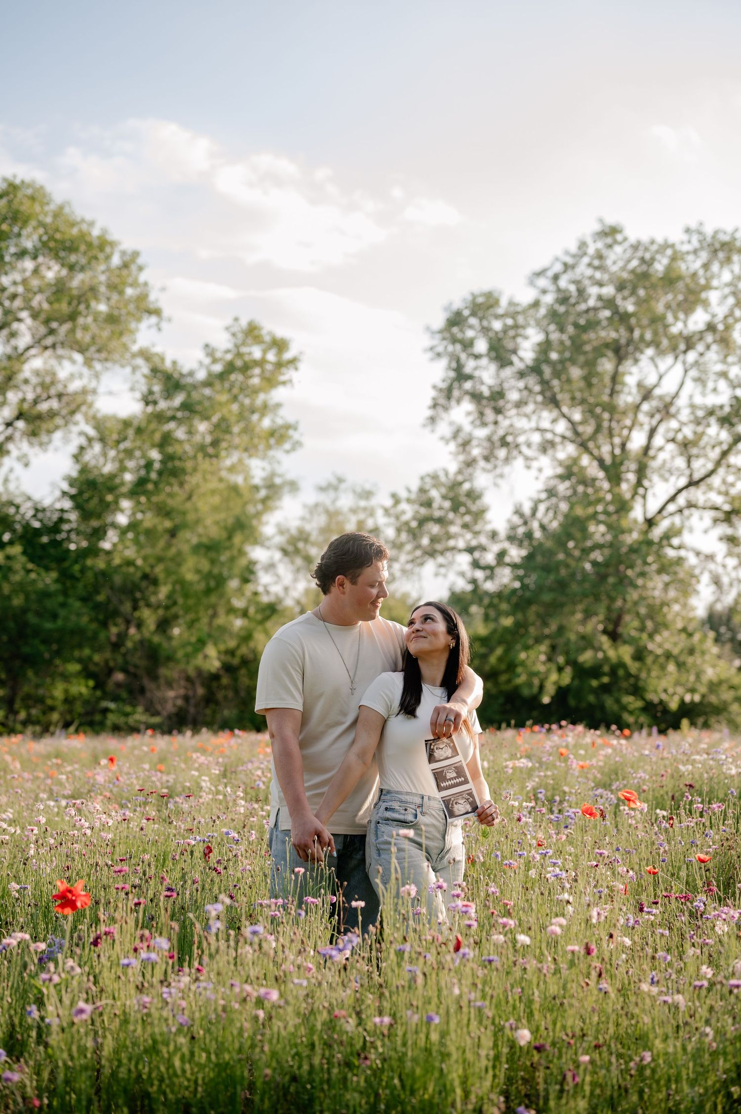 Couple standing in wildflowers with a sonogram for a Spring maternity announcement photo session in Richardson, TX