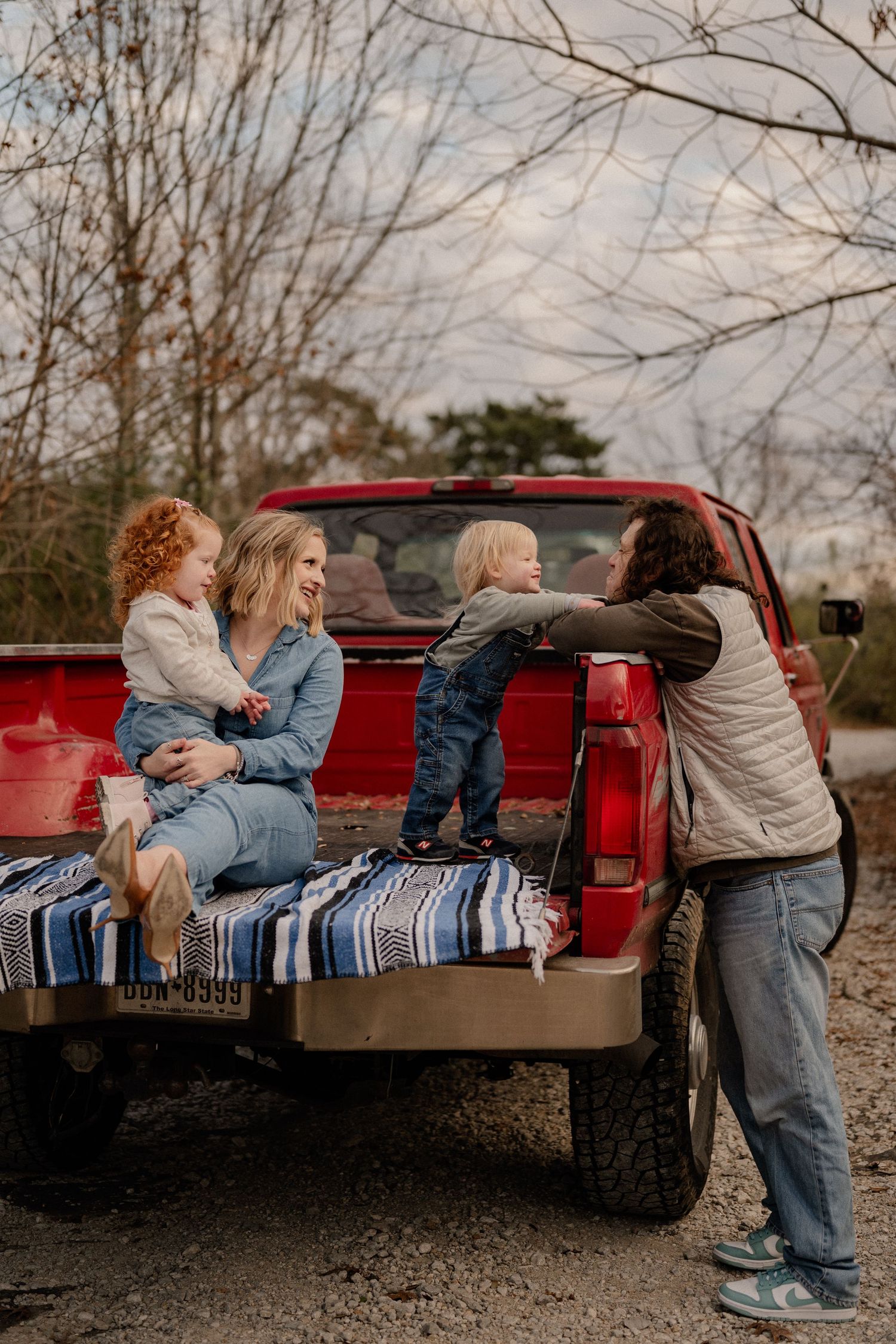 Family joyfully playing in the bed of a vintage red truck during an outdoor family photo session in Dallas, Texas