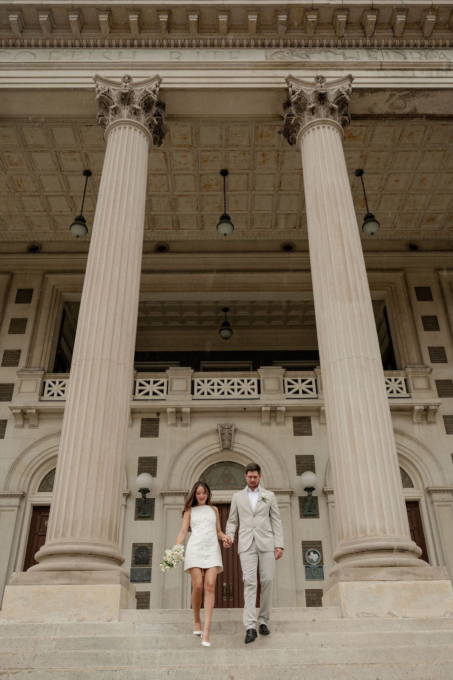 Couple walking down the steps of the large historical Dallas Scottish Rite building for their wedding portraits in Downtown Dallas, Texas