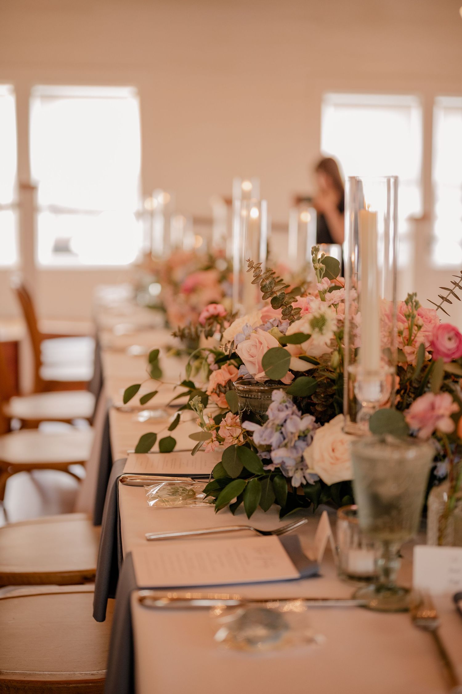Elegant table setting with pink and white floral centerpieces and tall white candles for a wedding reception.