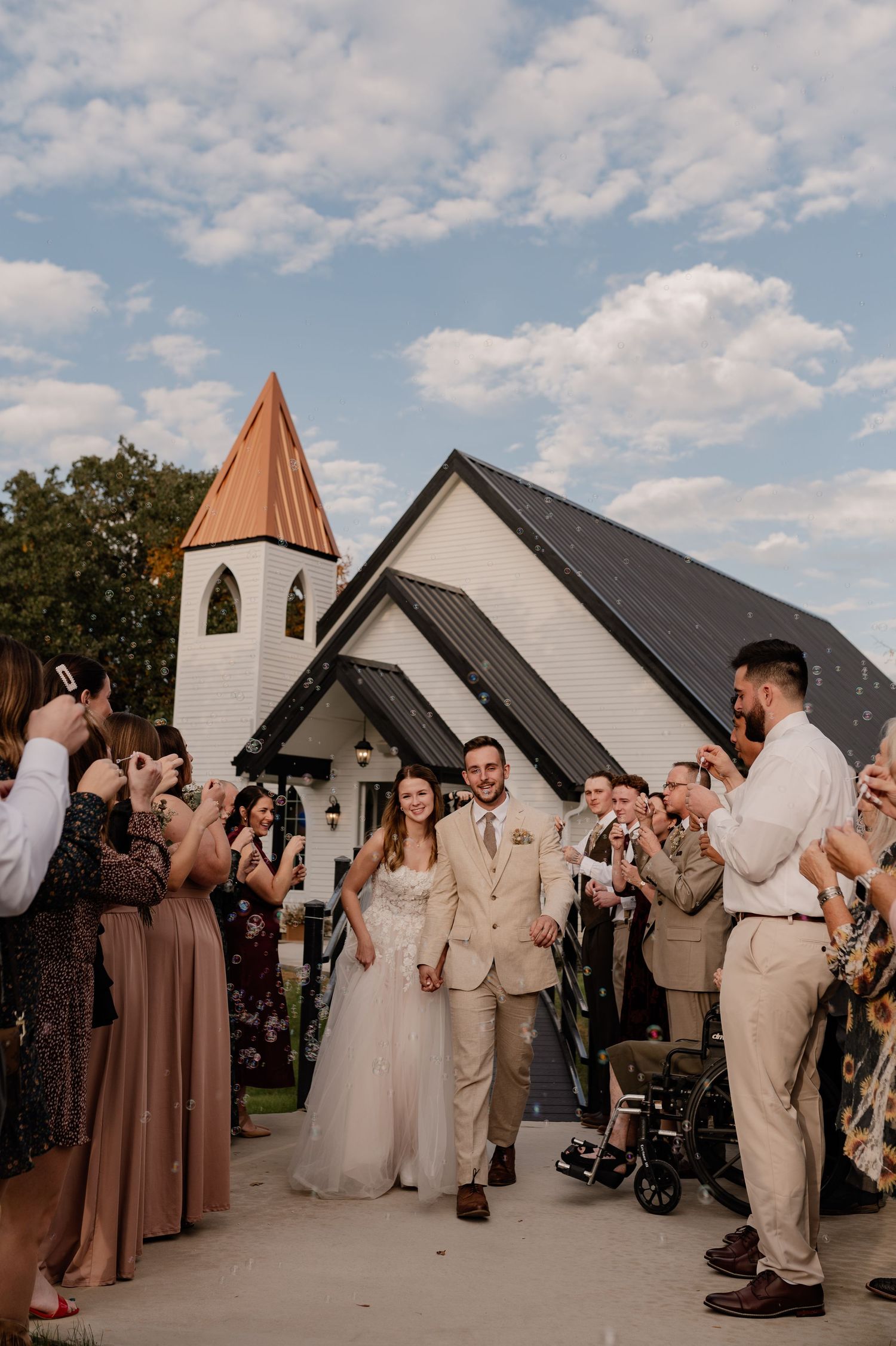 Bride and groom running through their ceremony bubble exit surrounded by friends and family in front of a white chapel in Denton, Texas