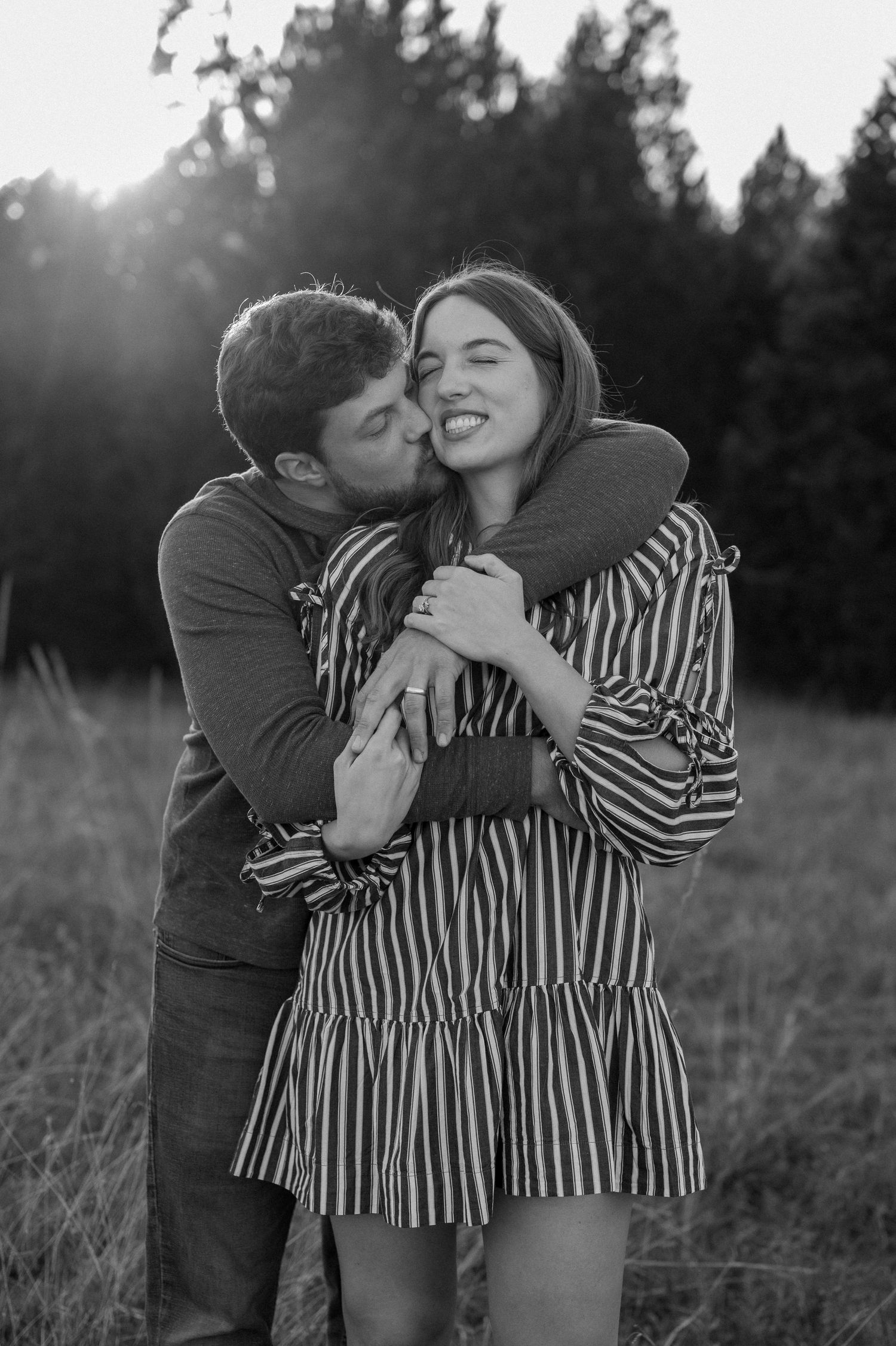 Black and white image of a married couple bear hugging during a casual fall couple session in a large tree lined field in during golden hour