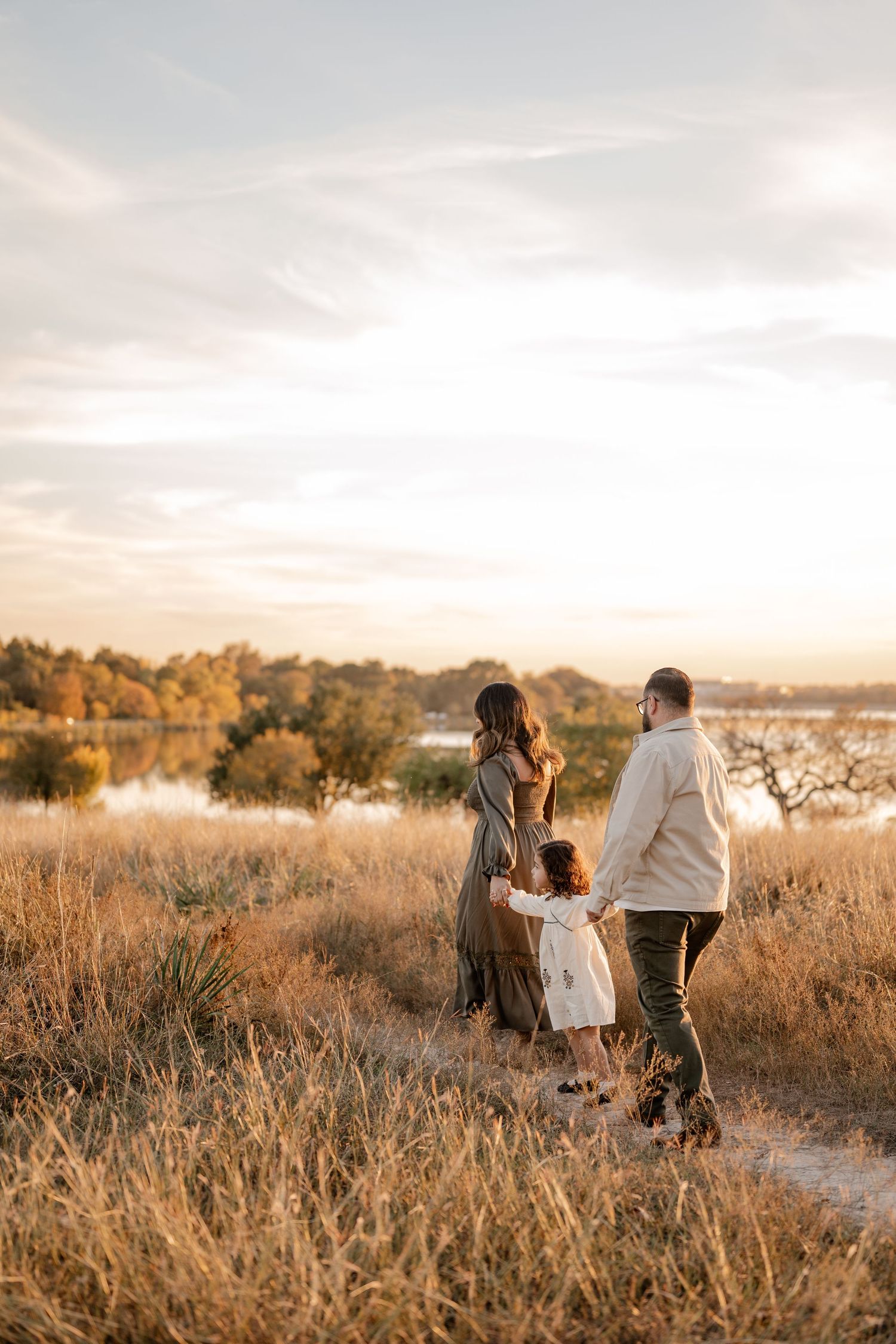 Candid photo of family casually walking through tall grass in a field overlooking the White Rock Lake in East Dallas, Texas