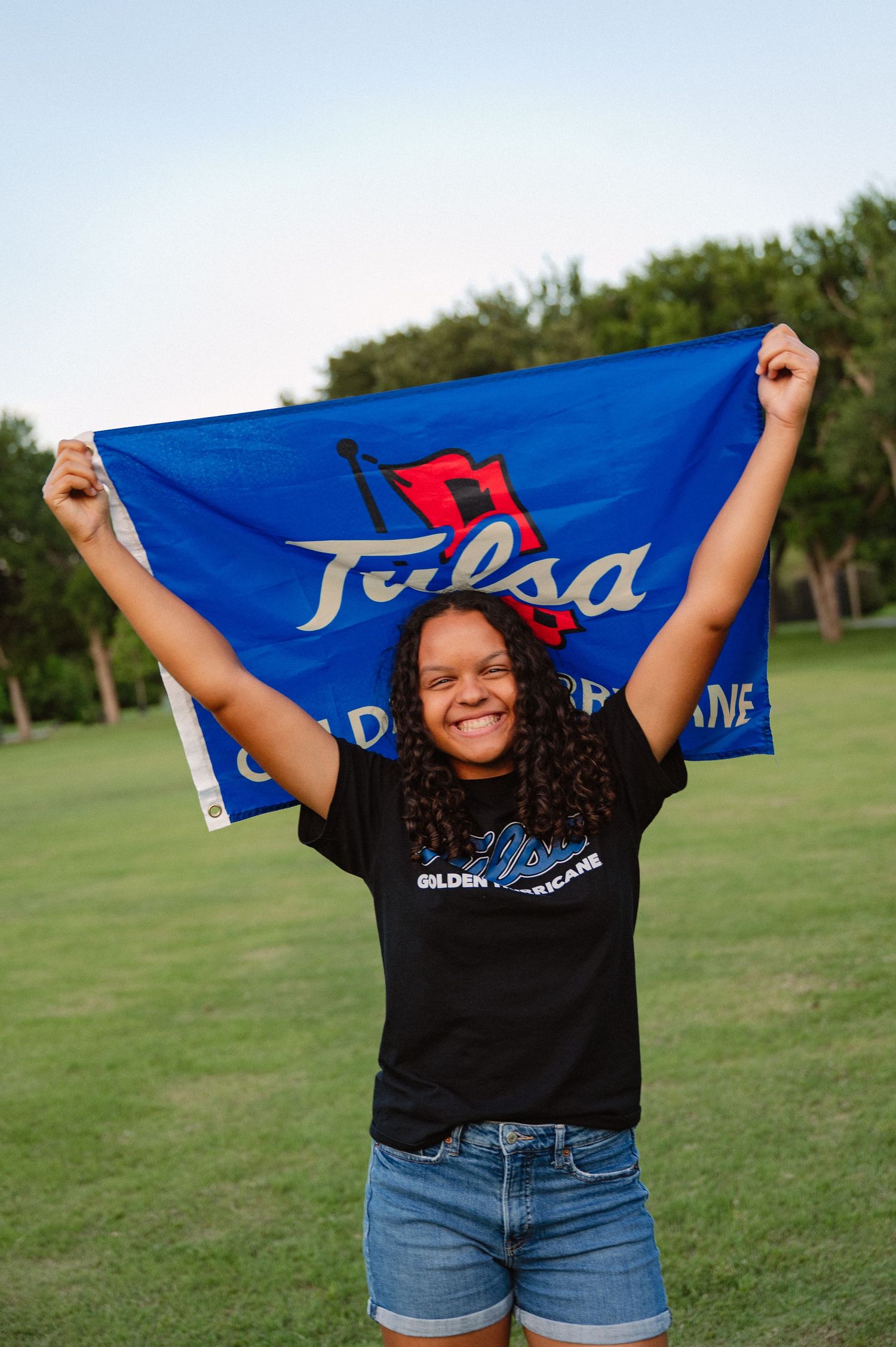 Senior holding a large banner for her college in a large tree-filled park in Richardson, Texas for a senior photo session