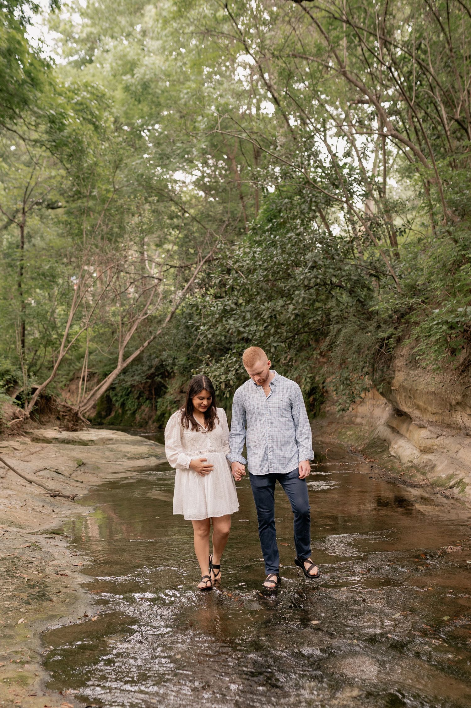 Expecting couple candidly walking through a small water way in Highland Park, Texas for their Spring maternity photo session
