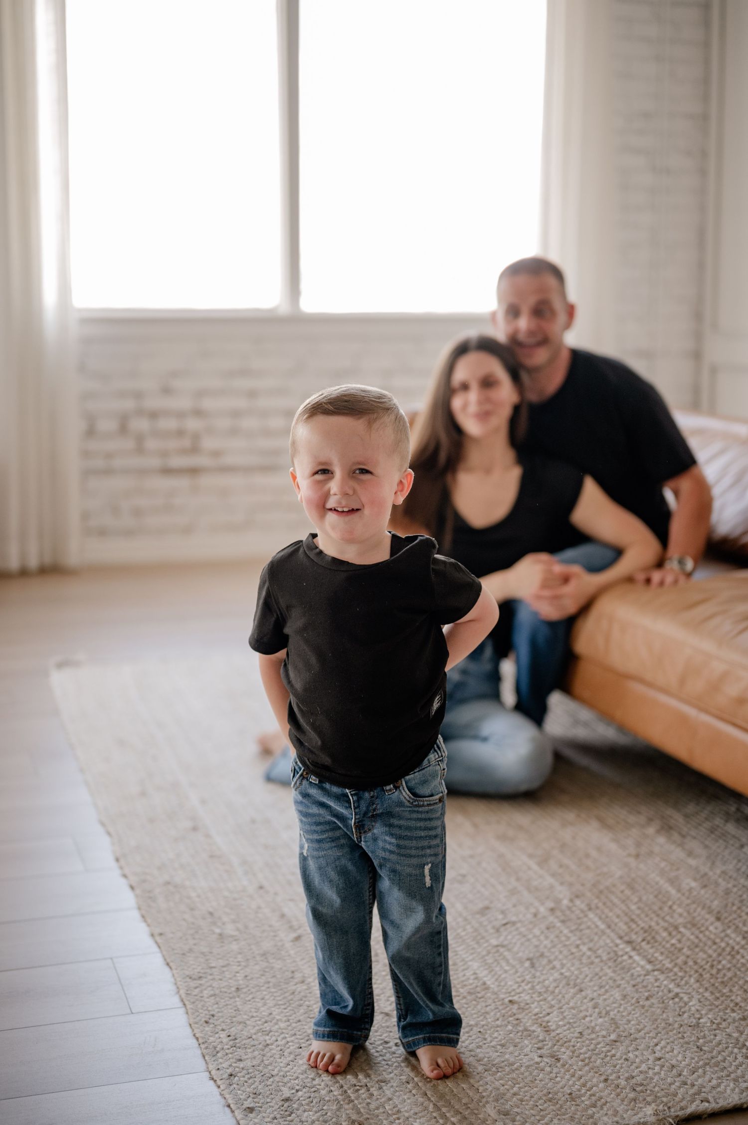 A toddler in black shirt with parents in the background at a bright studio in Dallas, Texas