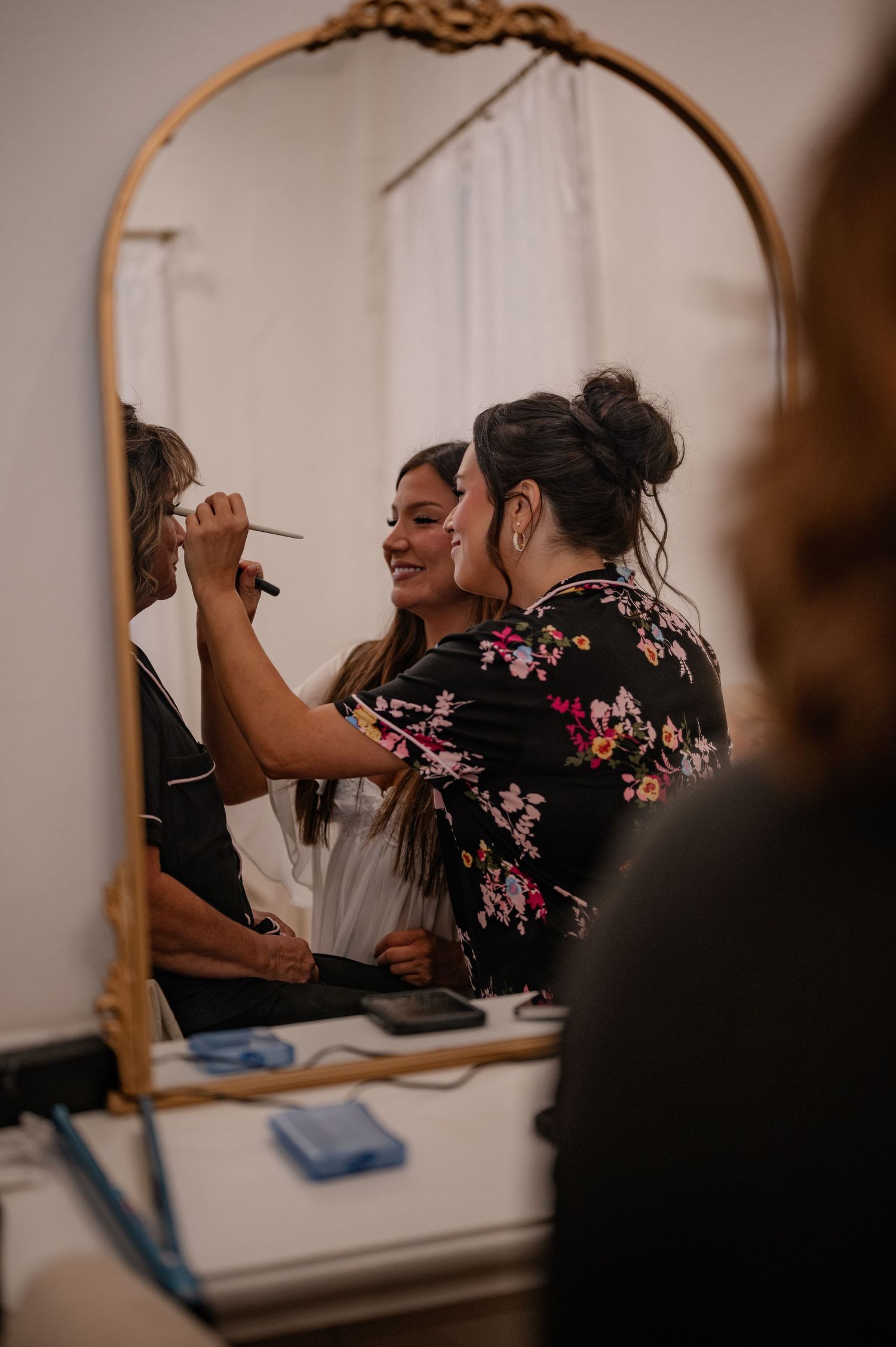 Bride & maid-of-honor doing the makeup of their mother while getting ready in a bridal suite before the ceremony in Natchitoches, Louisiana