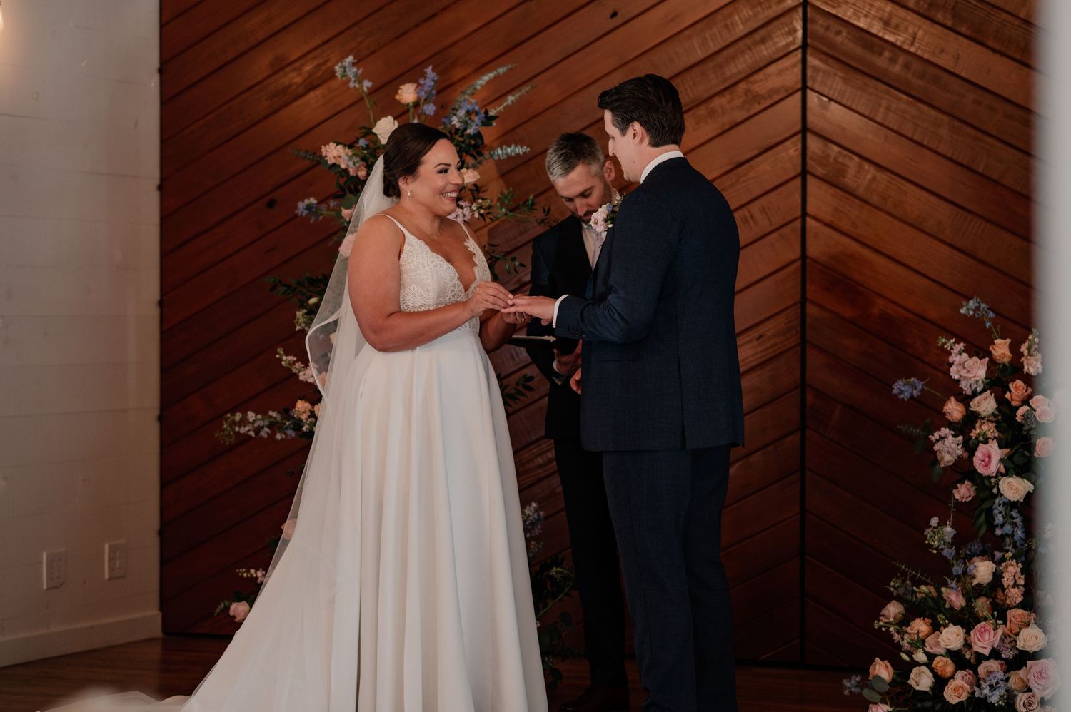 Wedding ceremony taking place in an elegant wood-paneled venue with floral arrangements.