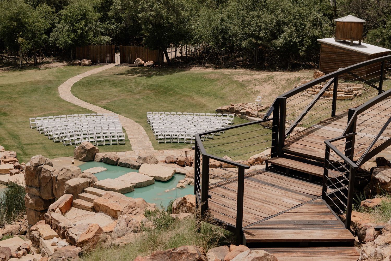 Outdoor wedding ceremony setup with white chairs arranged on a hillside near stone steps and waterfall.
