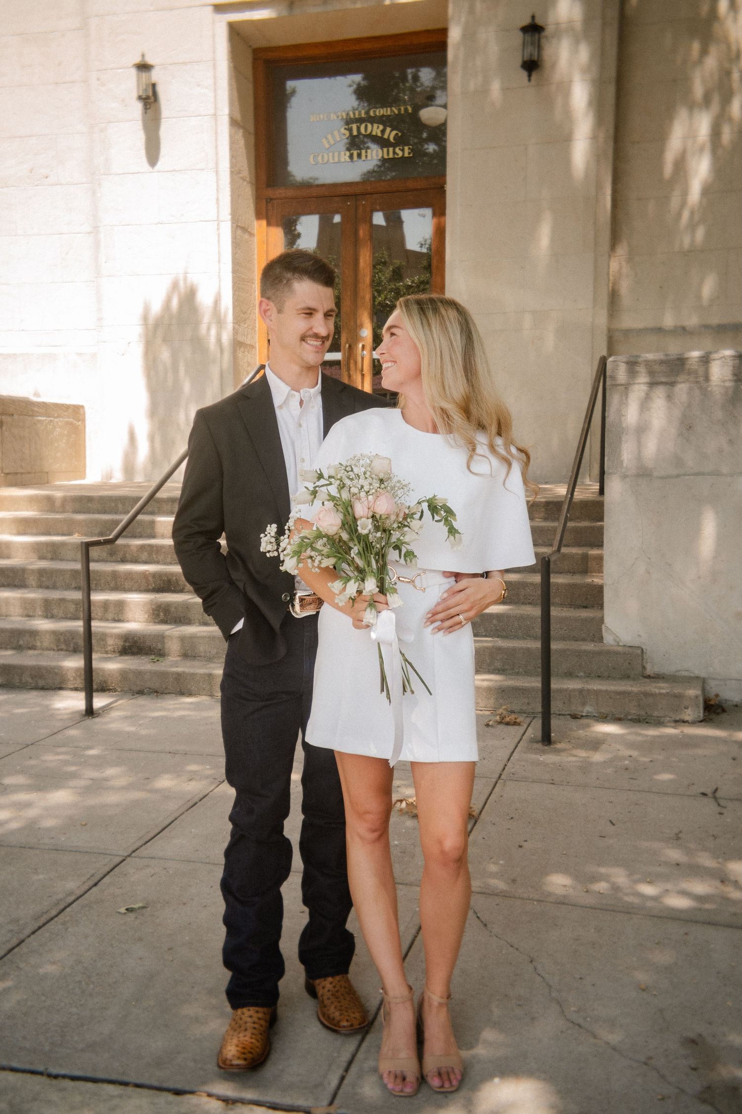 Film photo of couple posing in front of a staircase outside of the downtown Rockwall courthouse during elopement wedding photo session