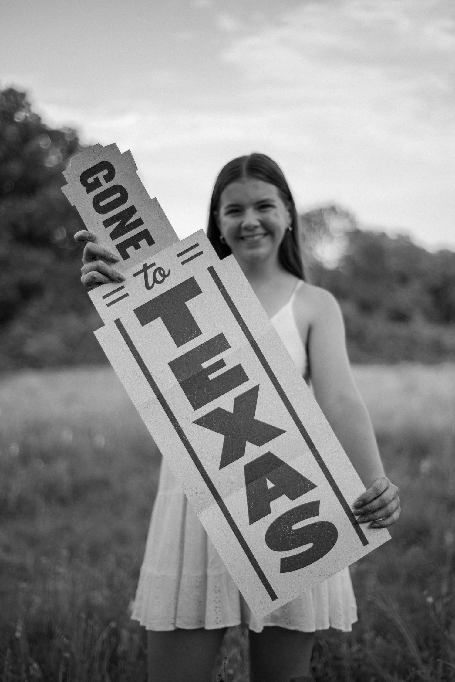 Senior girl posing in wildflowers holding a University of Texas sign for a Spring senior photo session in Richardson, Texas