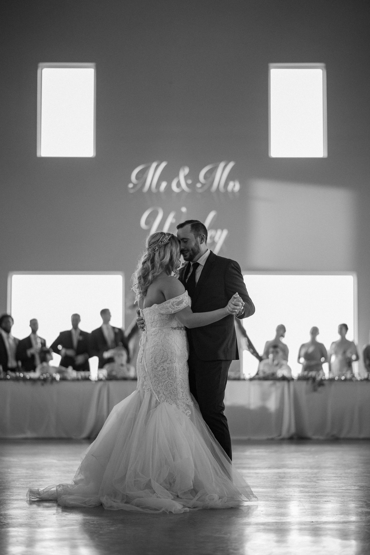 Black and white photo of bride and groom intimately dancing in a large wedding reception hall for their first dance