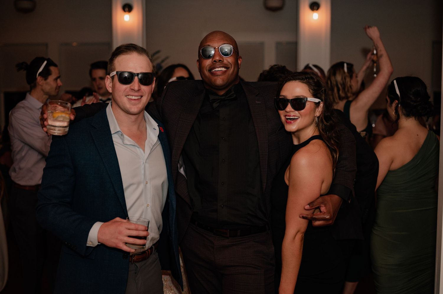 Three party guests in sunglasses posing together at wedding reception