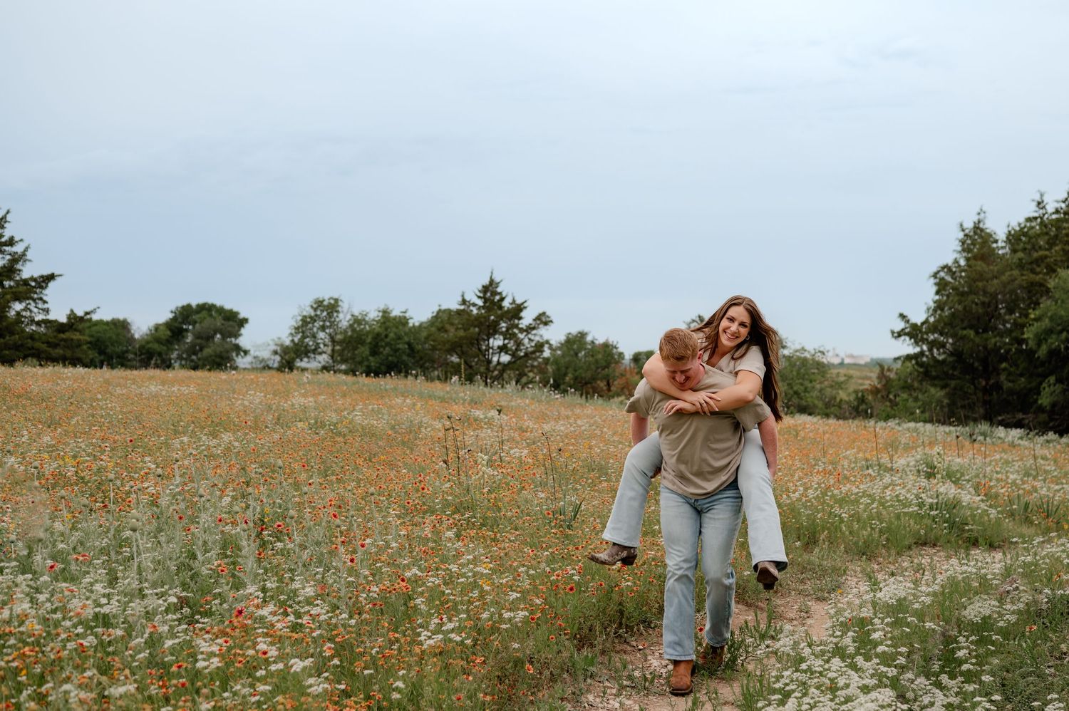 A couple laughs joyfully as a man gives a woman a piggyback ride through a blooming wildflower meadow in Fort Worth, Texas