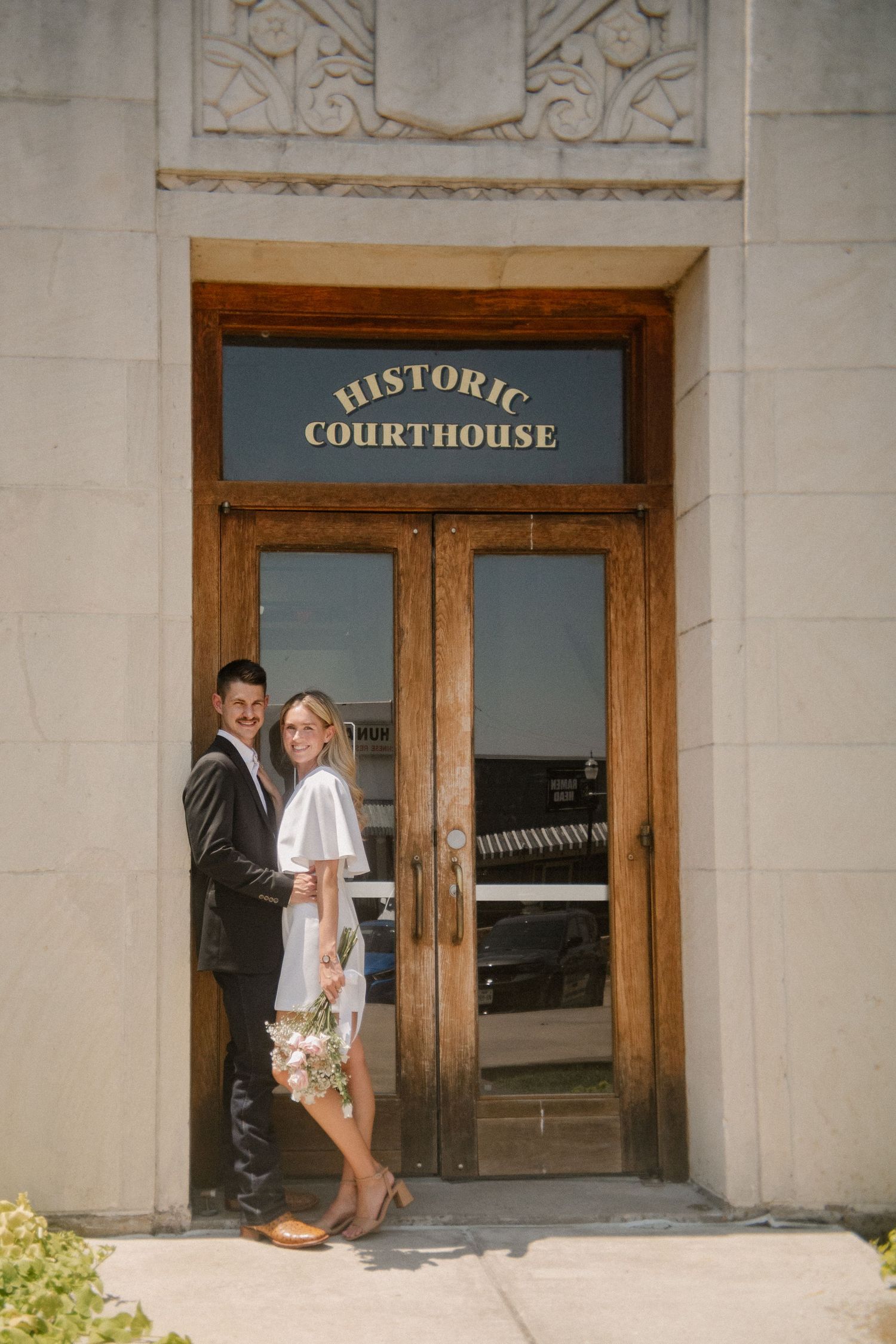Film photo of couple posing outside in front of the downtown Rockwall courthouse during a summer elopement wedding photo session