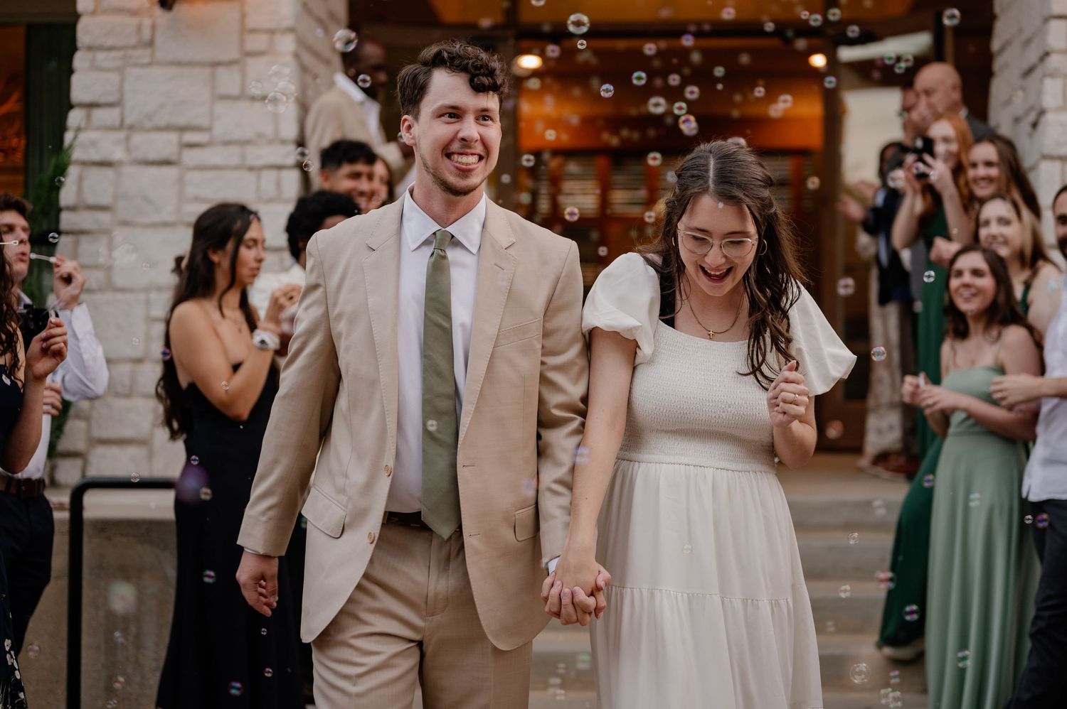 Wedding couple leaving their reception with a grand exit lined with friends and family blowing bubbles in the background