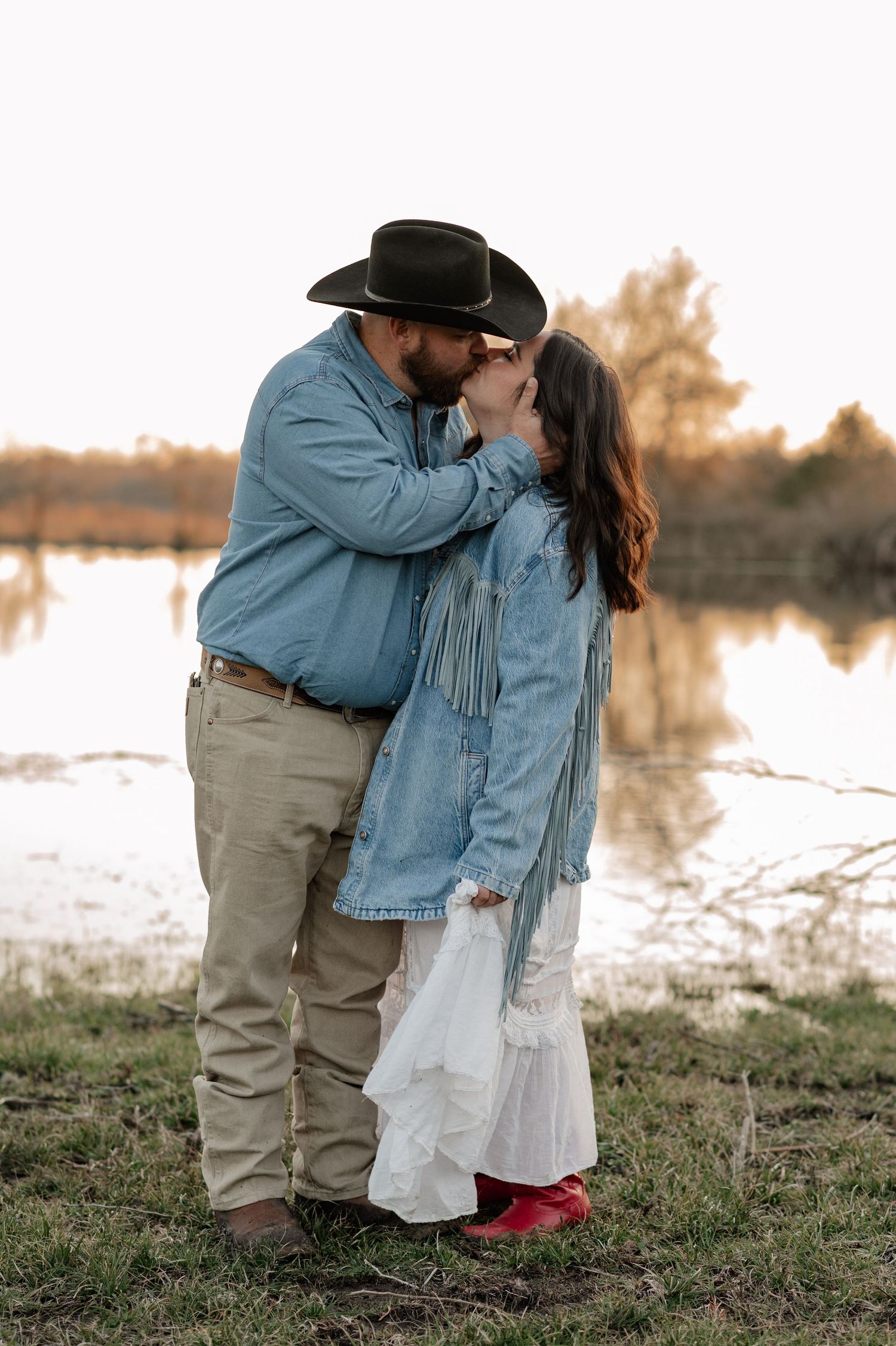 Couple intimately embracing and kissing for an at-home family session in front of a large pond on their farm in Greenville, TX