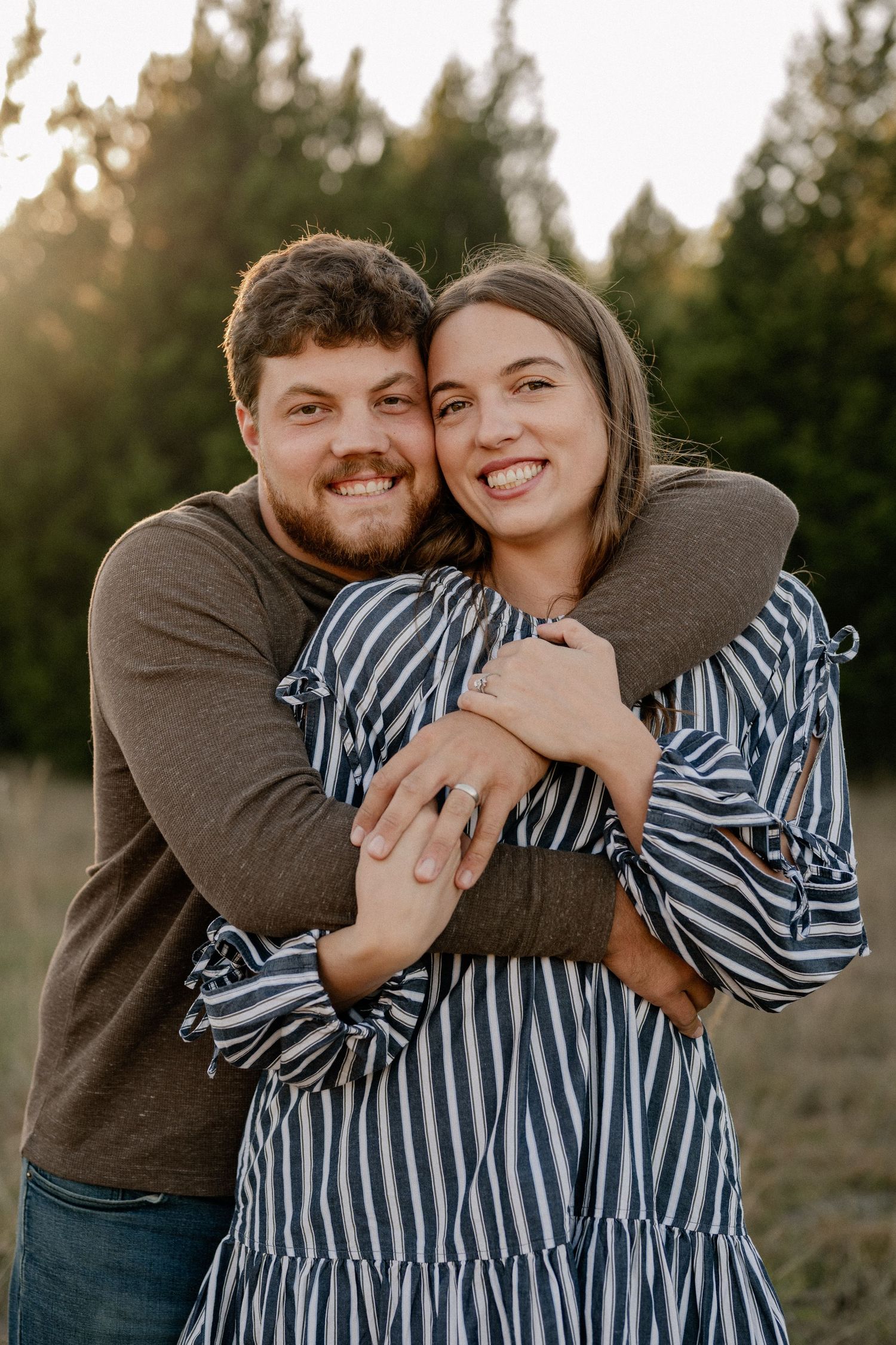 Married couple bear hugging during a casual fall couple session in a large tree lined field in during golden hour
