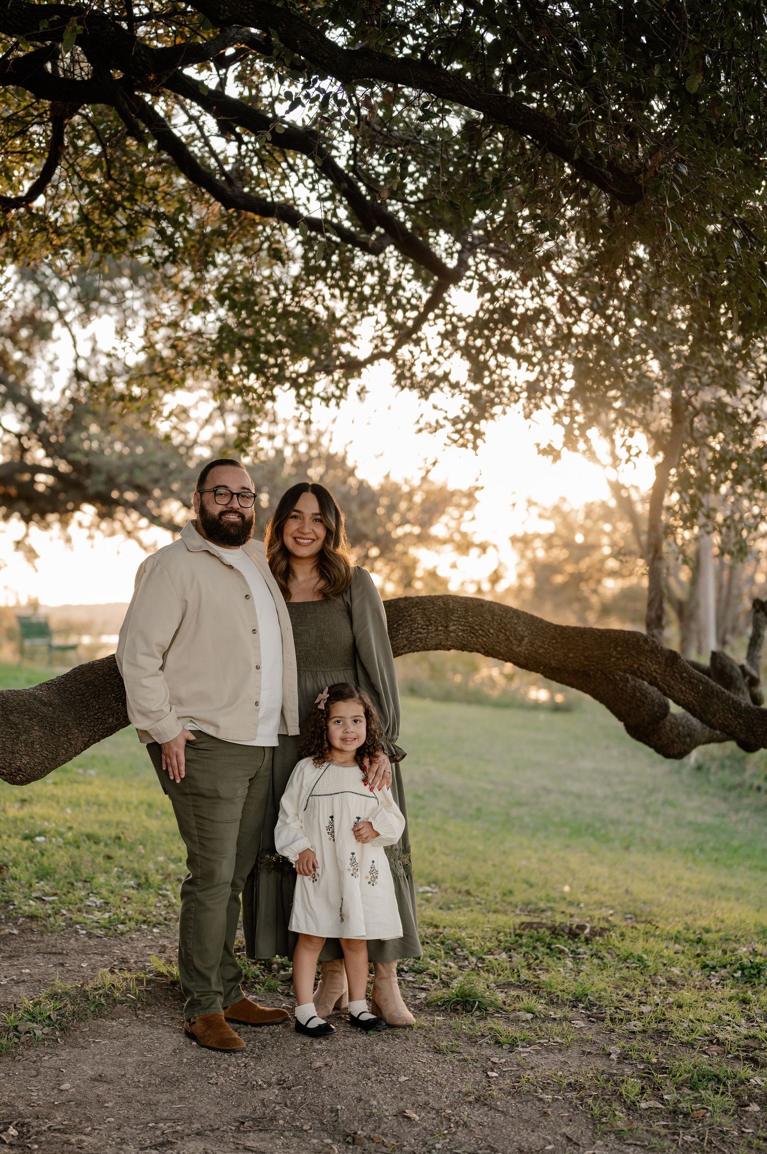 Family smiling & standing in front of an old tree with White Rock Lake at sunset in the background for a winter family photoshoot in Dallas