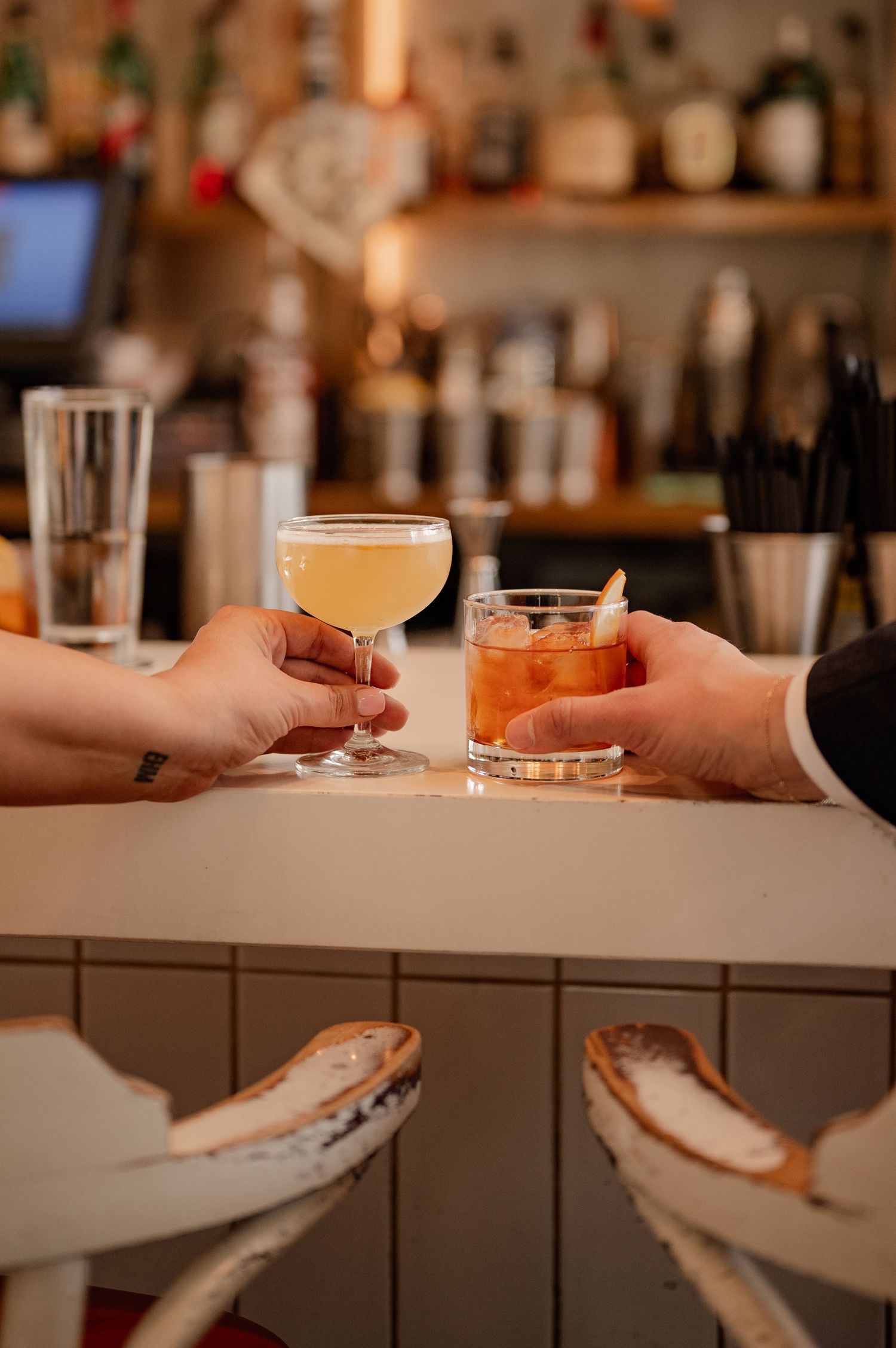 Two cocktails being served on white bar counter with bar stools.
