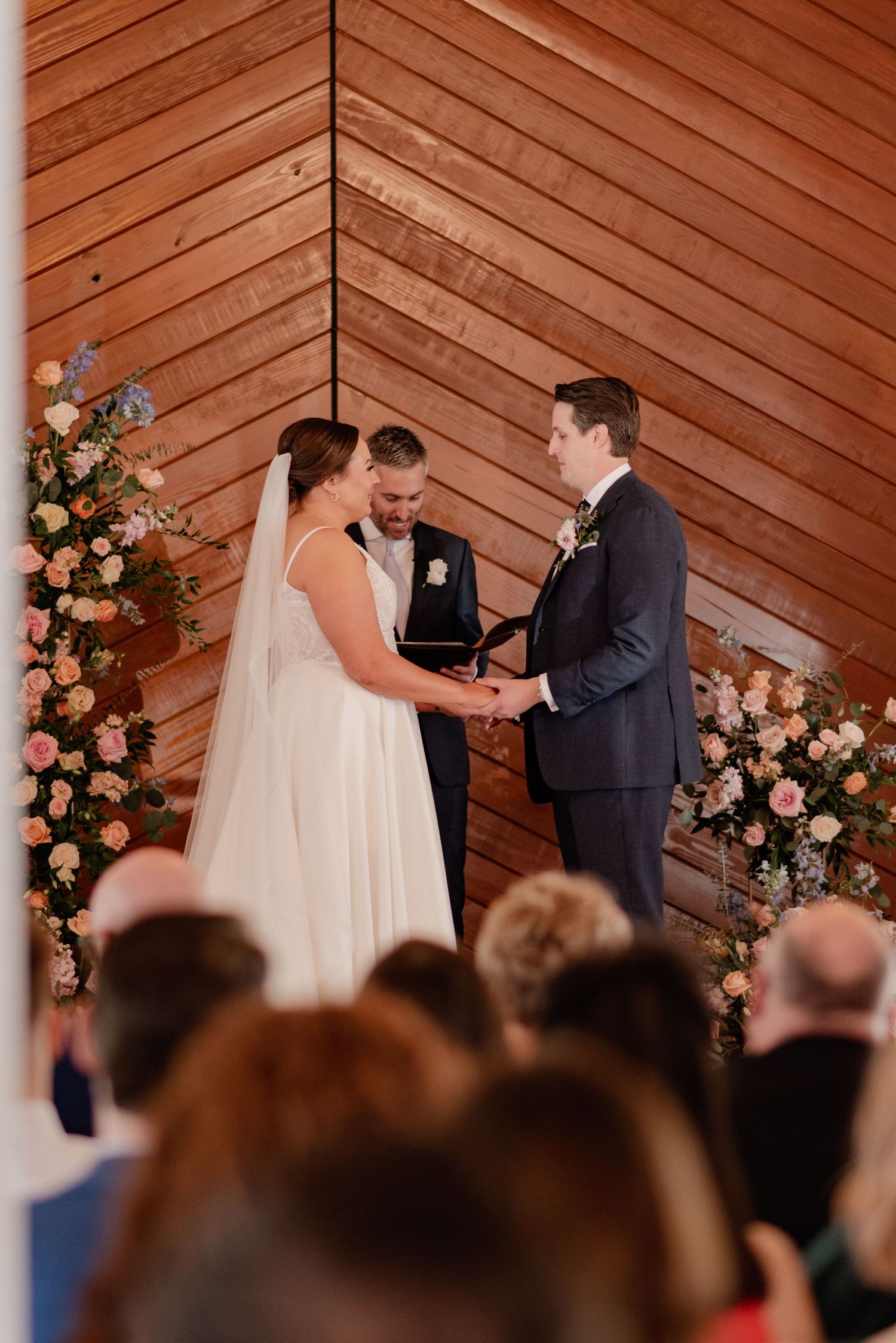 A wedding ceremony takes place in a vintage wooden chapel with floral arrangements framing the altar area.