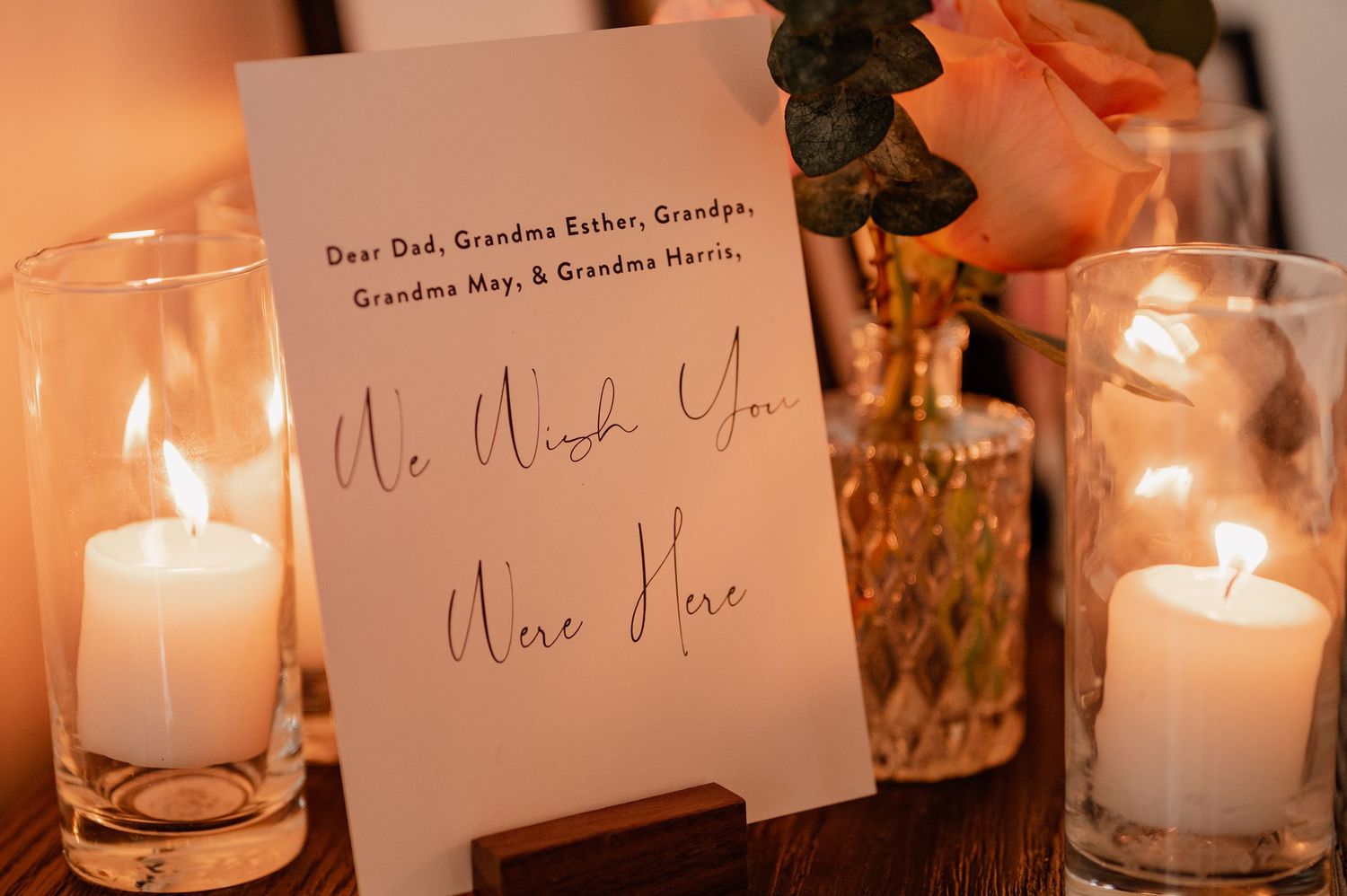 Handwritten wedding note card displayed between lit candles in glass holders.