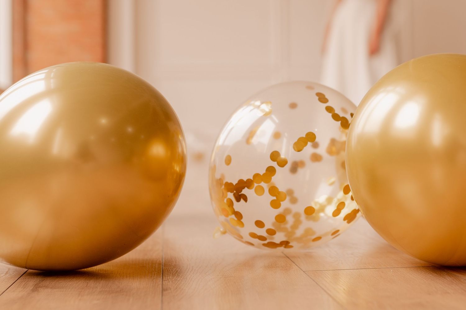 Row of gold and white balloons with confetti on neutral background.