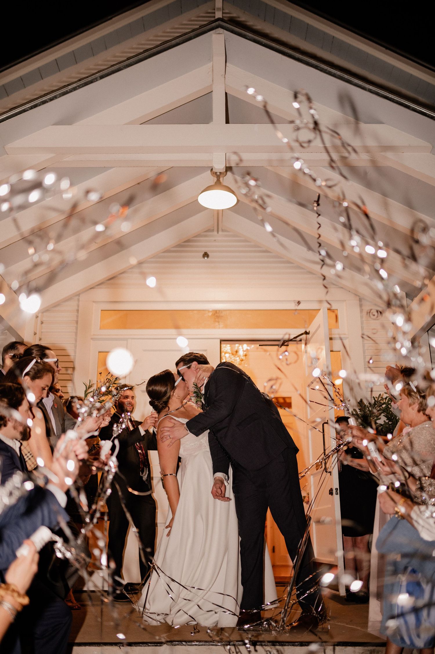 Wedding couple kissing before lively exit from wedding reception with guests popping streamers outside of Bishop Arts venue in Dallas, Texas