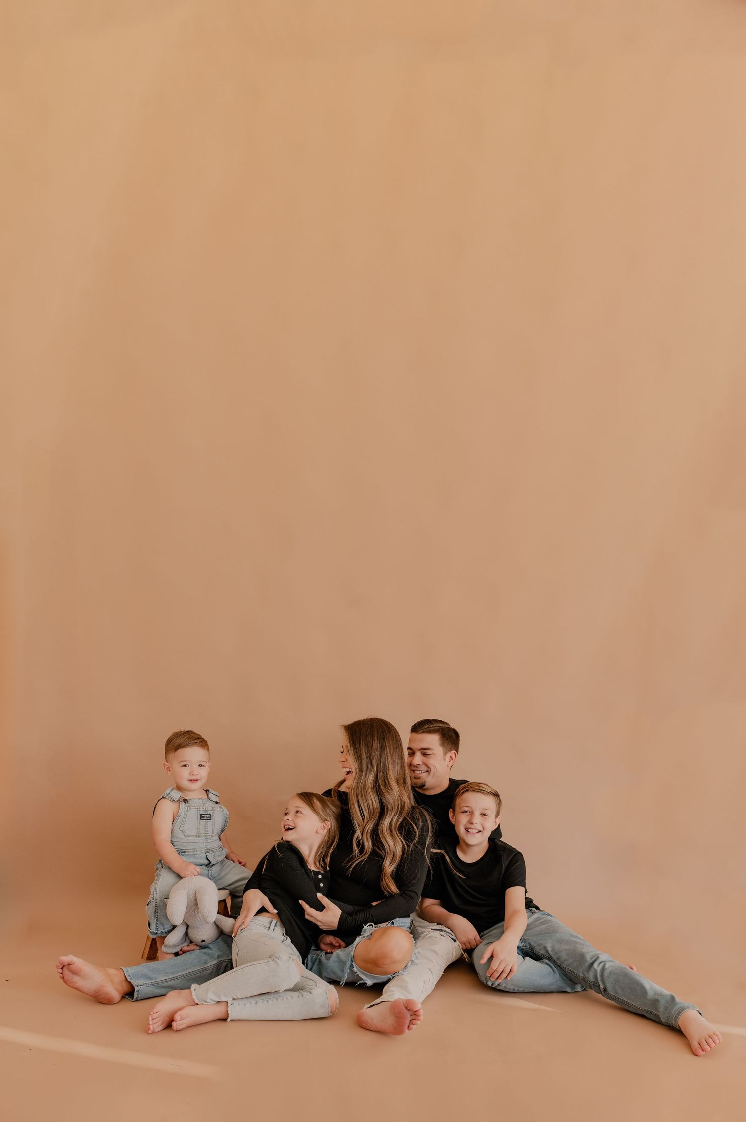 Family candidly laughing at each other while sitting on a tan paper backdrop at The Photo Space studio during a family photo session
