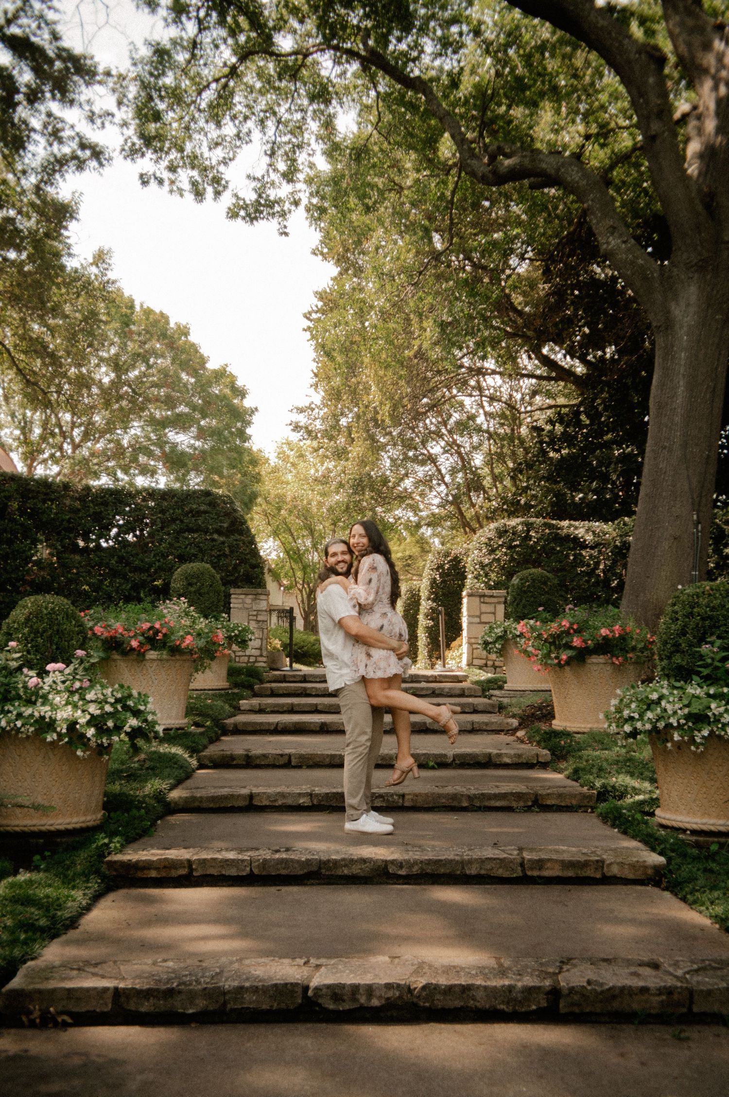 Couple joyfully embracing and laughing during a proposal couple's session at the Dallas Arboretum in East Dallas