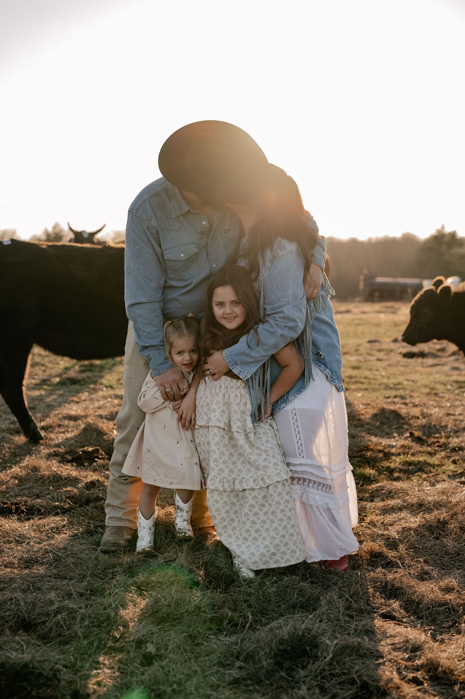 Family of four posing with the mom and dad kissing on a cow farm in Rockwall, Texas for a fall at-home family session