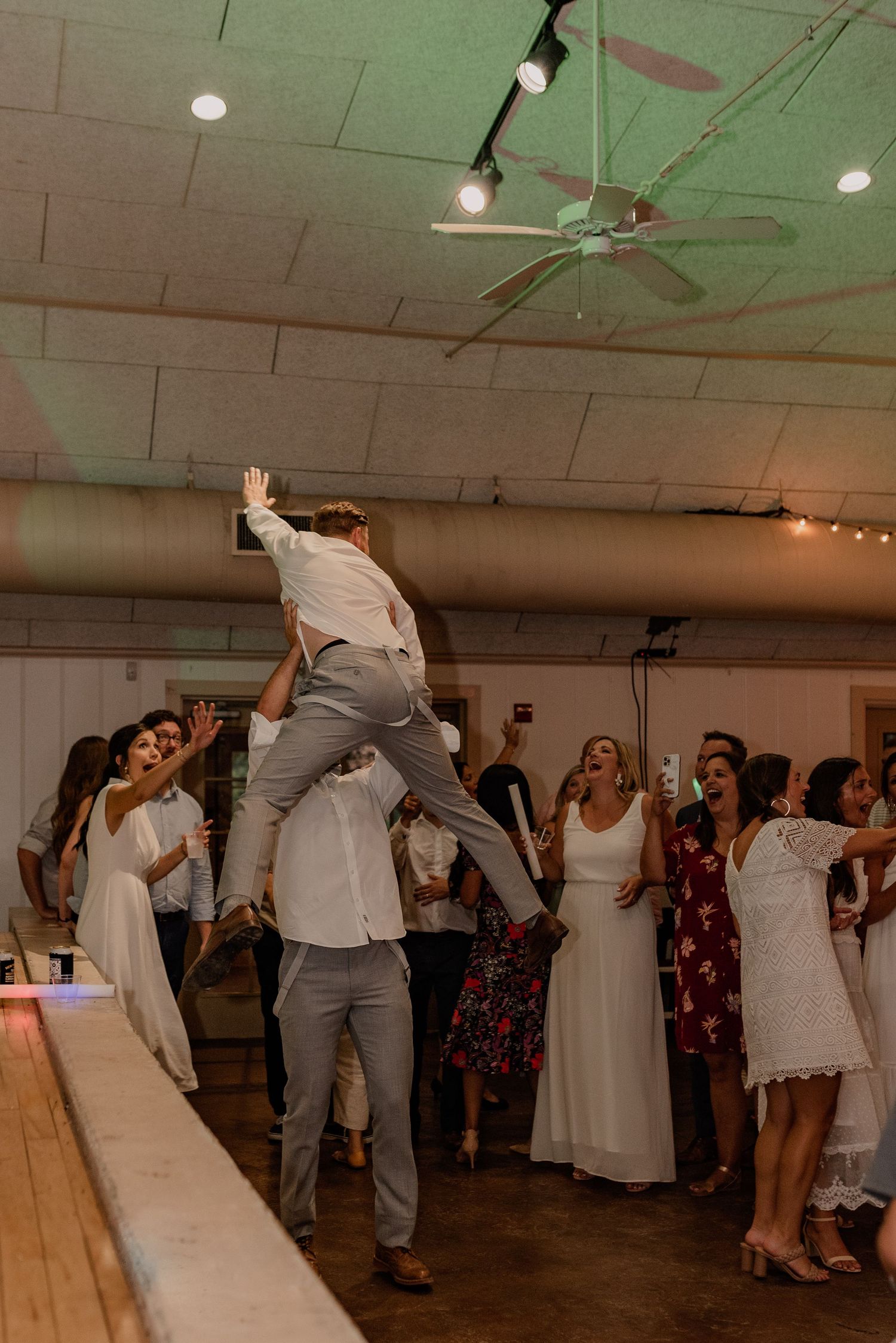 Guest performs acrobatic dance move at wedding reception while others cheer.