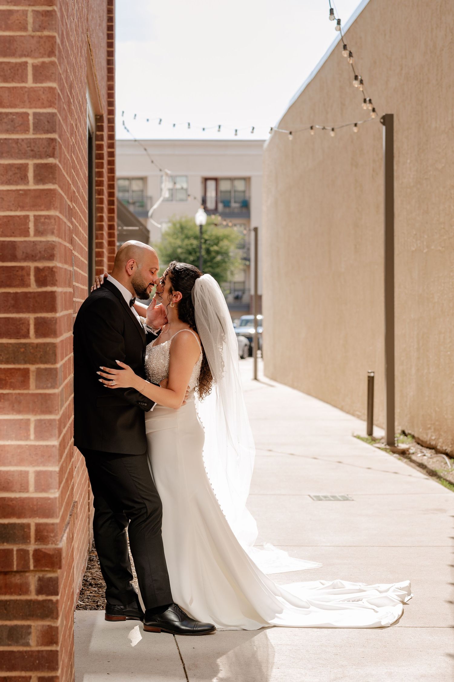 Bride and groom intimately kissing in a downtown alley against a brick wall in the bright sun near Plano, Texas