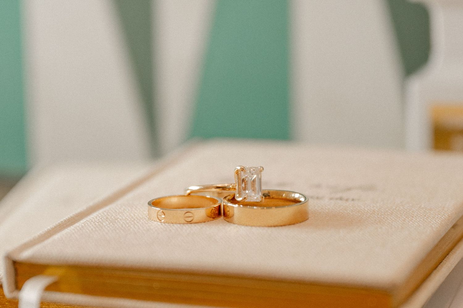 Wide shot of wedding rings and bands resting on top of each other on a vow book in a golden light to document wedding details