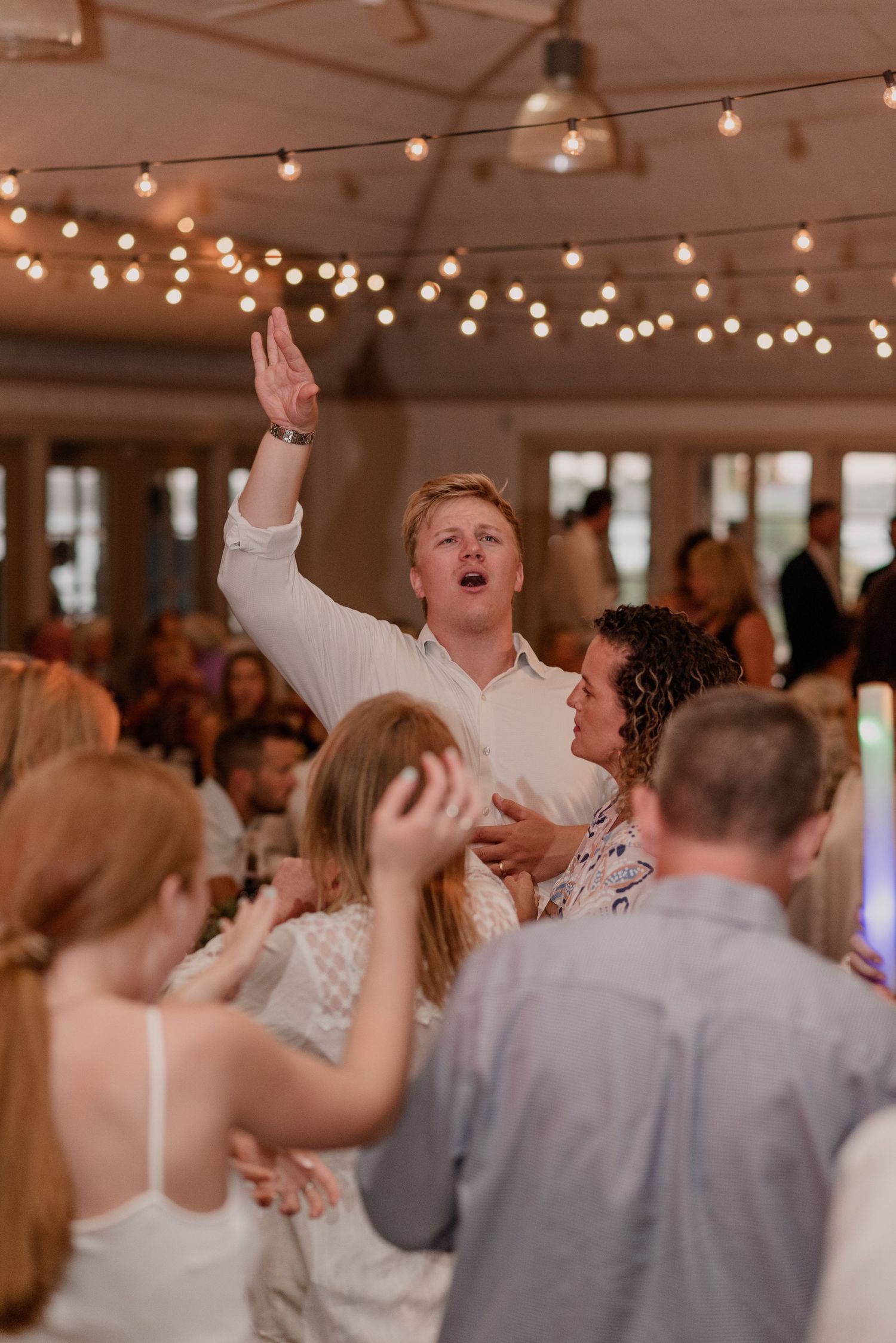 Energetic dancing and celebration at wedding reception under warm string lights.
