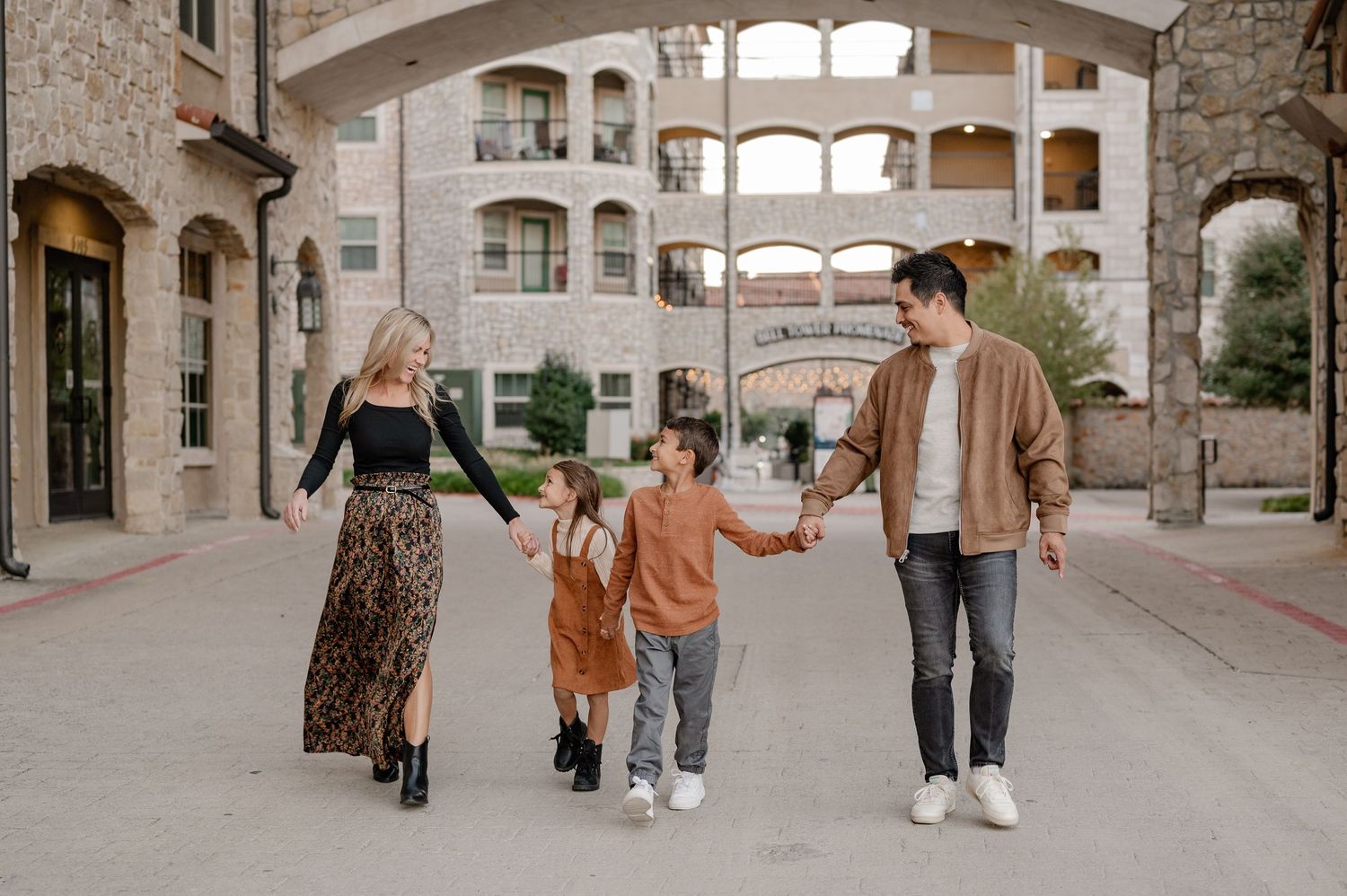 Family of 4 candidly holding hands walking through a Croatian inspired Adriatica Village for a Fall family photo session in McKinney, Texas
