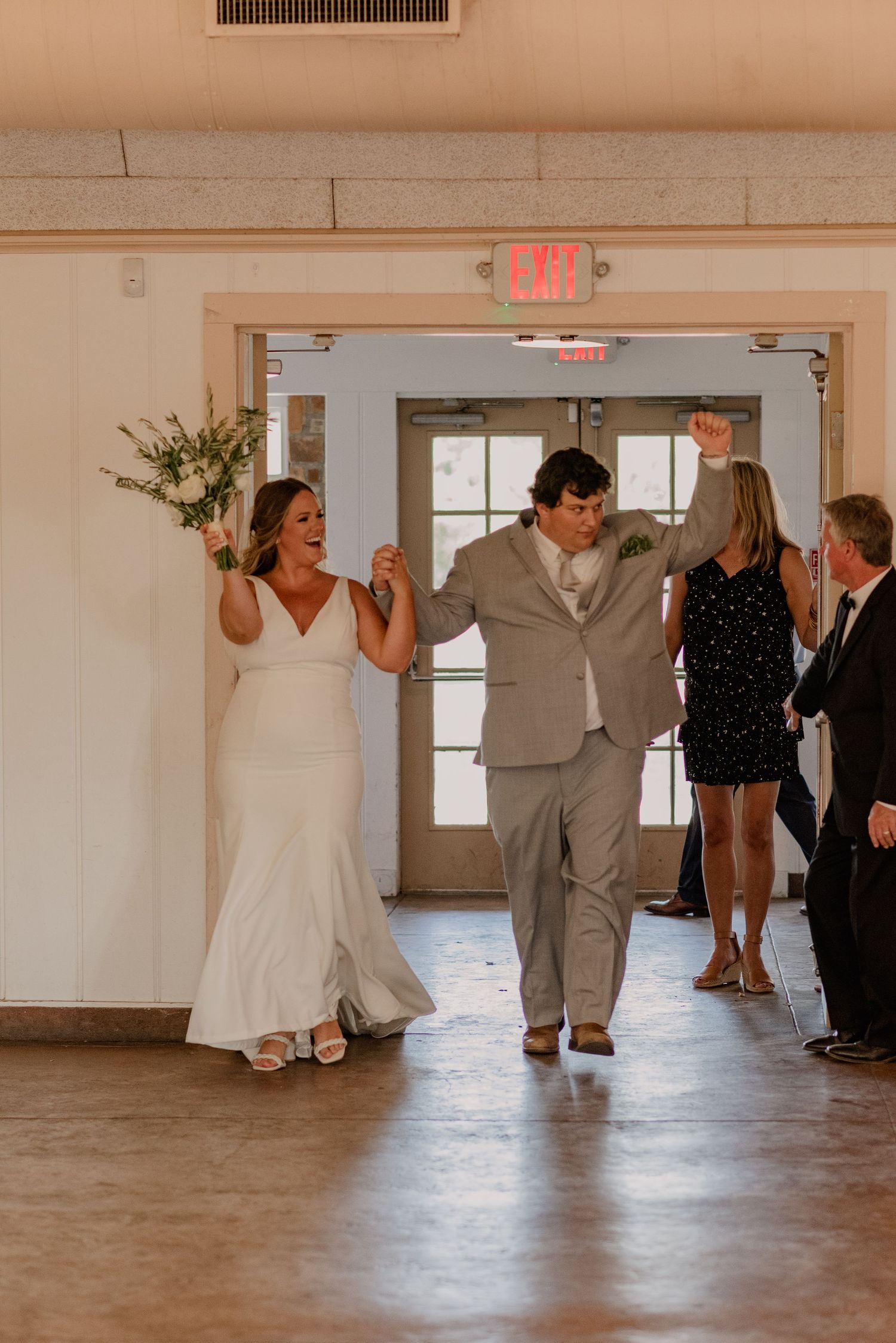 Wedding party dances in a spacious indoor venue with wooden floors and natural lighting.