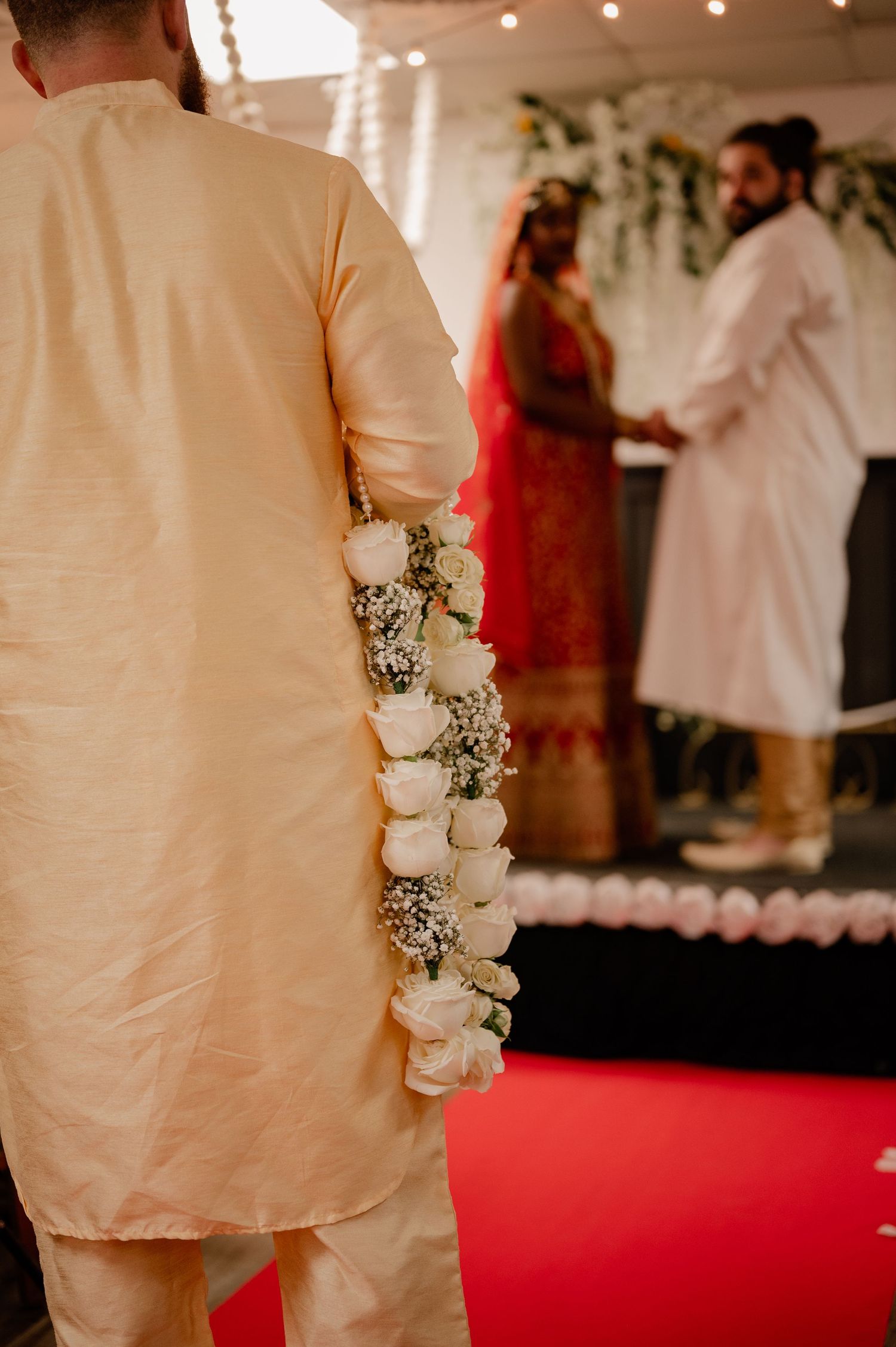 Wedding celebration on a red carpet with white floral decorations and elegant attire.