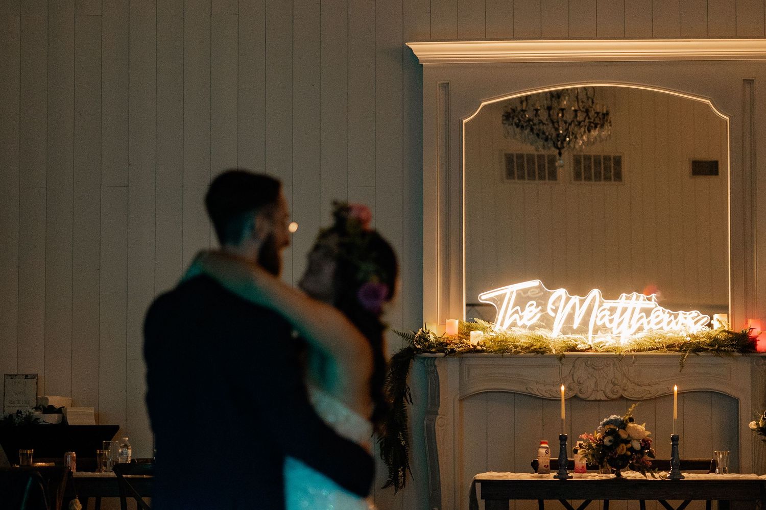 Moody photo of bride and groom blurred in the foreground of a neon sign intimately dancing in a dark reception hall for their first dance