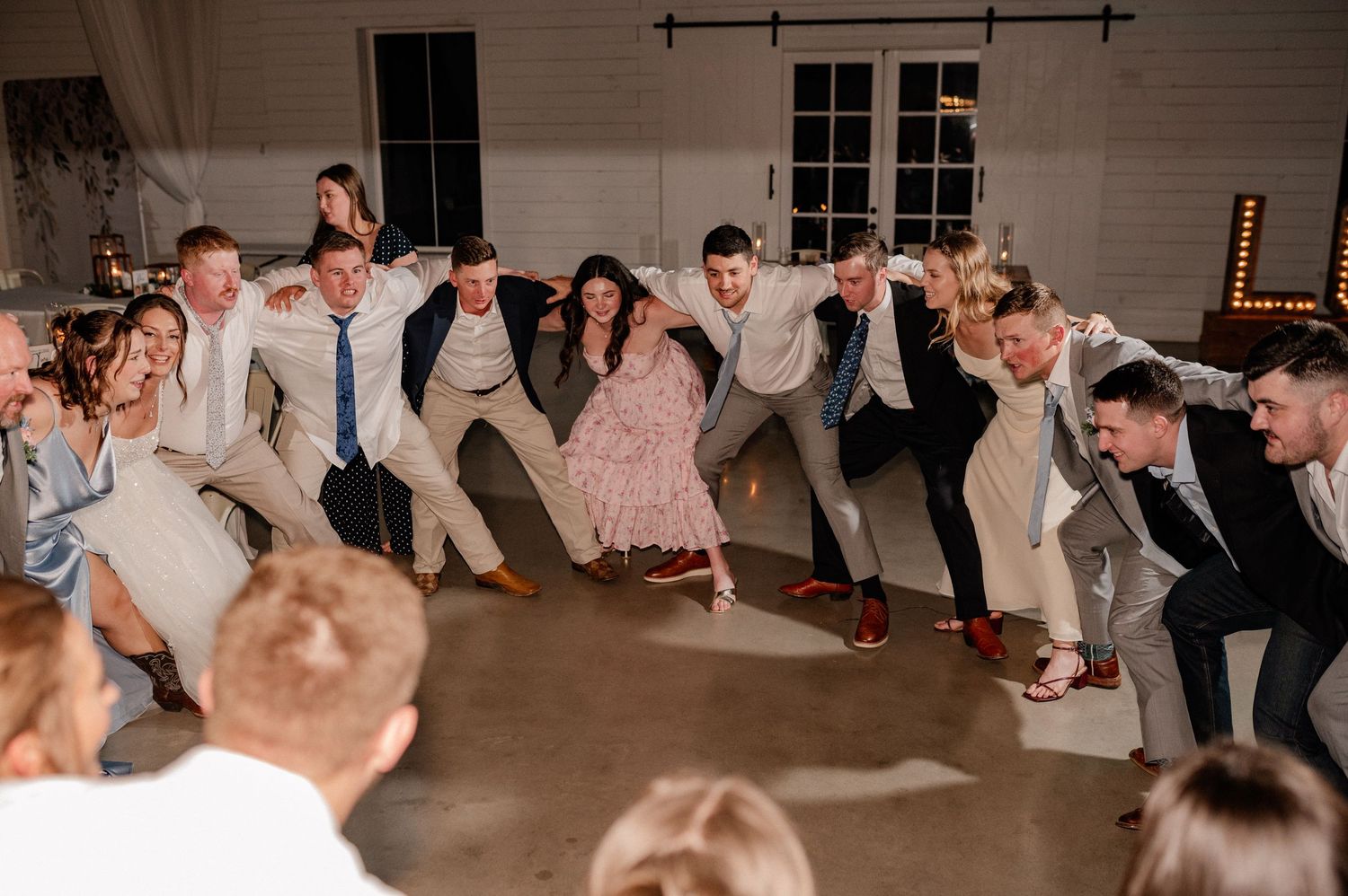Texas A&M graduates interlocking arms in a circle for the Aggie War Hymn in a moody wedding reception hall