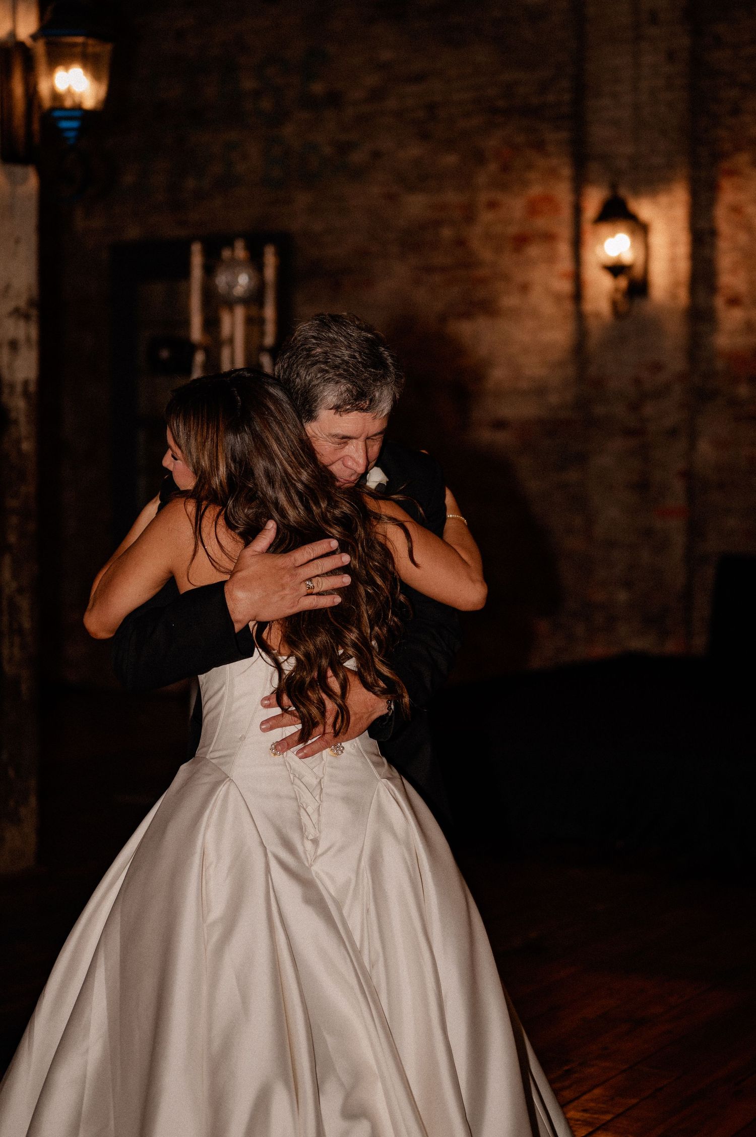 Candid moment of bride hugging her father in a dark and moody Louisiana reception venue after their father daughter dance