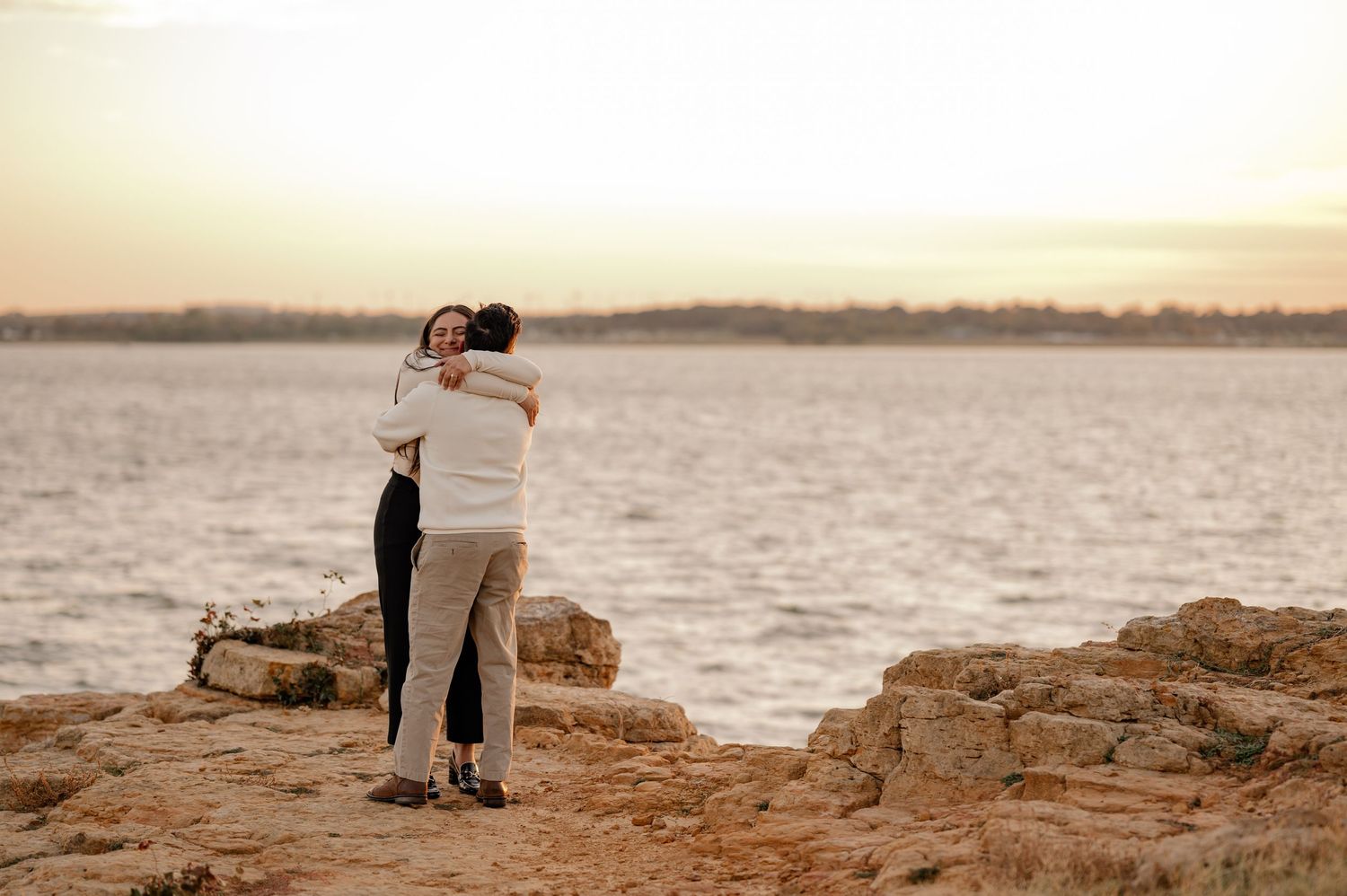 Couple joyfully embracing after their surprise proposal on a rocky cliff in Grapevine, Texas at golden hour