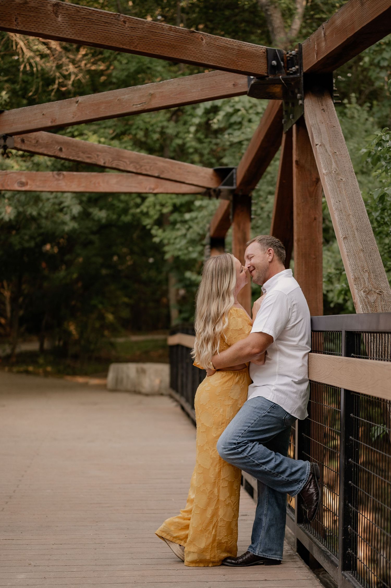 Couple intimately cuddled up and kissing on a large wooden bridge at Prairie Creek Park in Richardson, TX for summer engagement photos