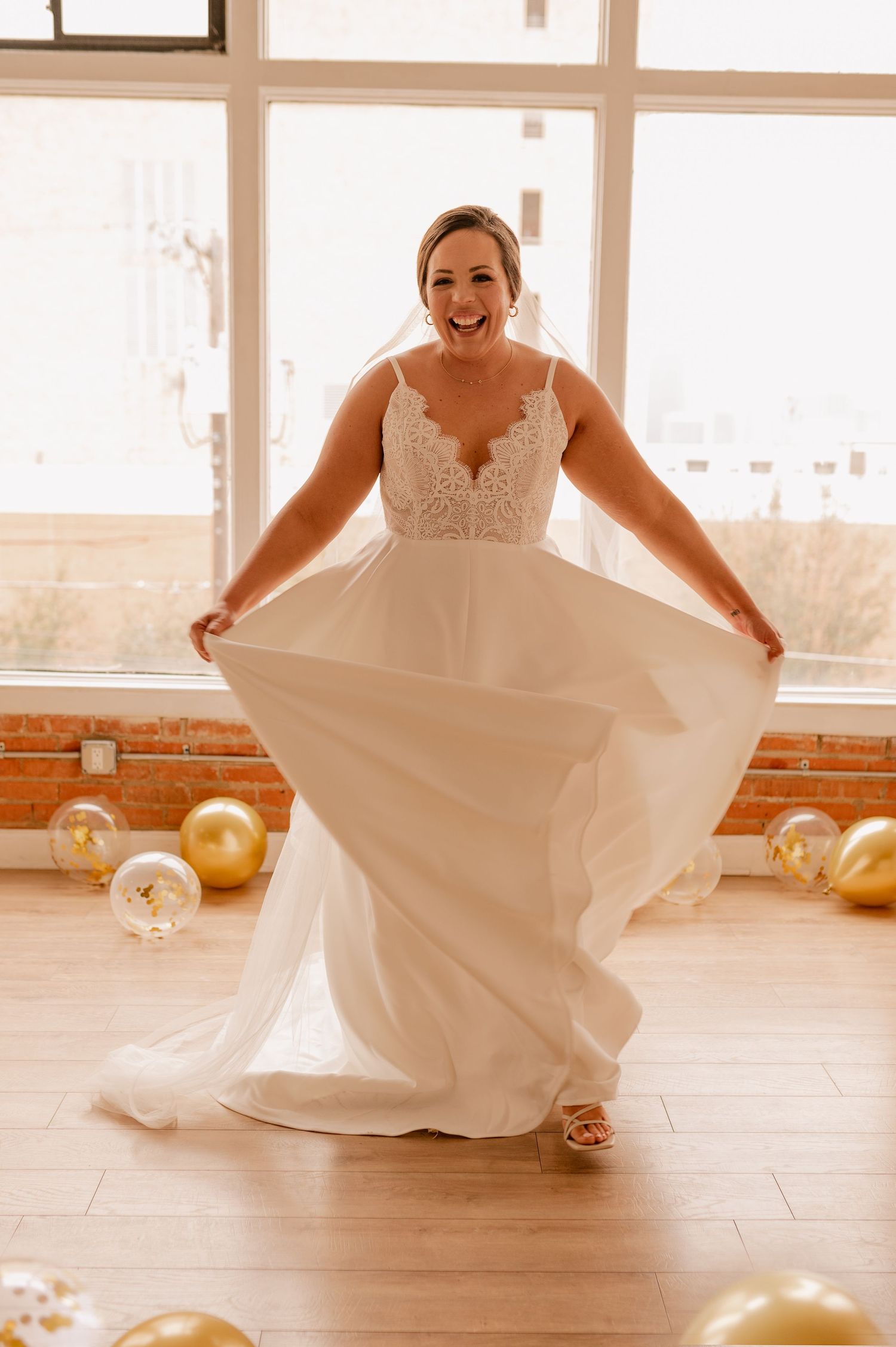 Joyful bride dancing in flowing white dress among golden balloons on hardwood floor.