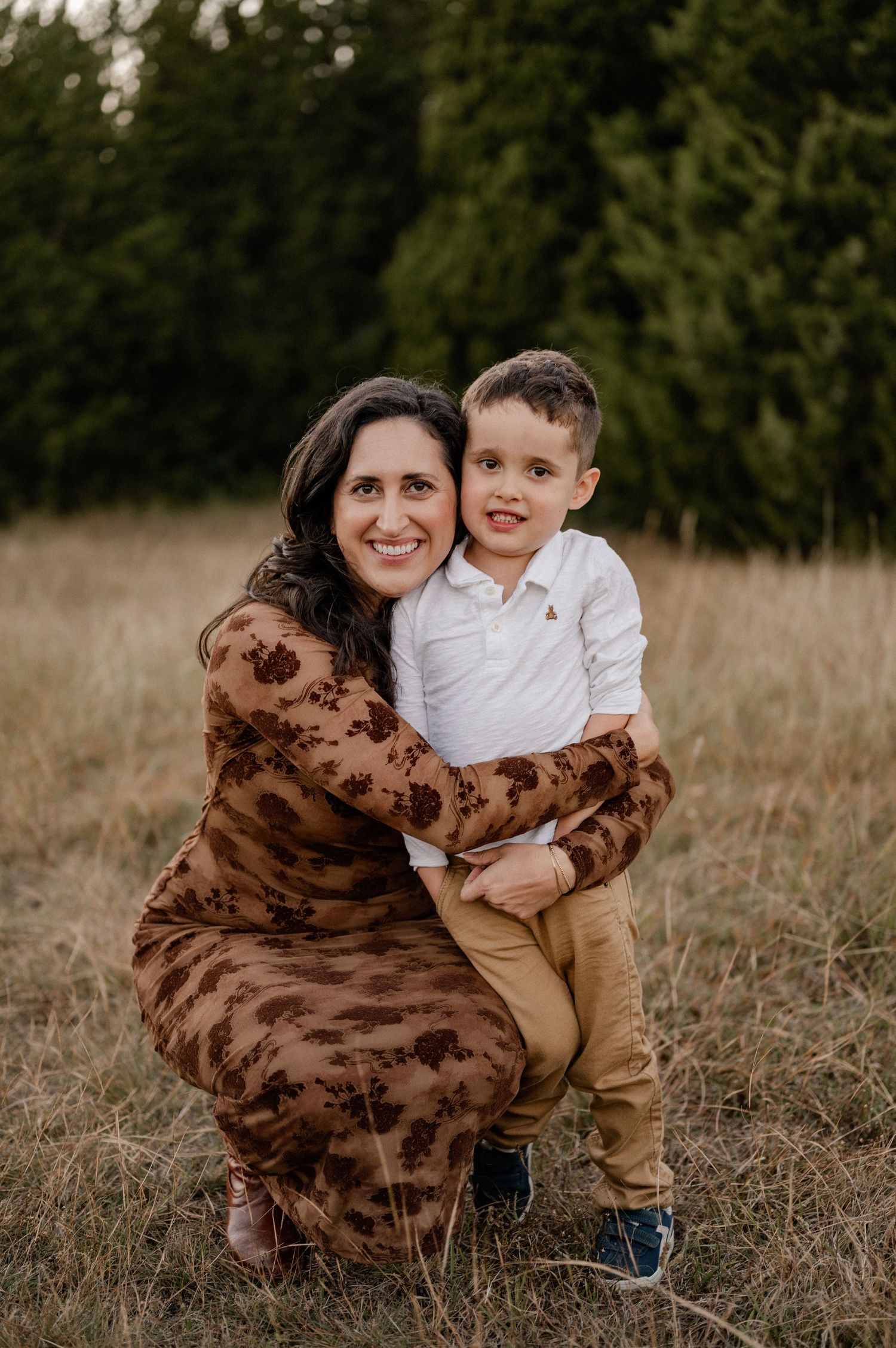 Mother embracing her son in a large field lined with trees at an outdoor family session for fall photos in Sunnyvale, Texas