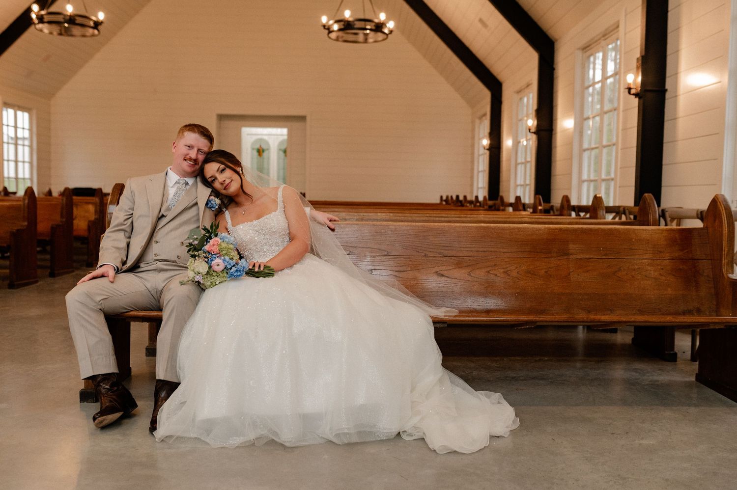 Romantic photo of Bride and groom sitting in a rustic pew in a moody chapel during wedding couple portraits at venue in Paradise, Texas