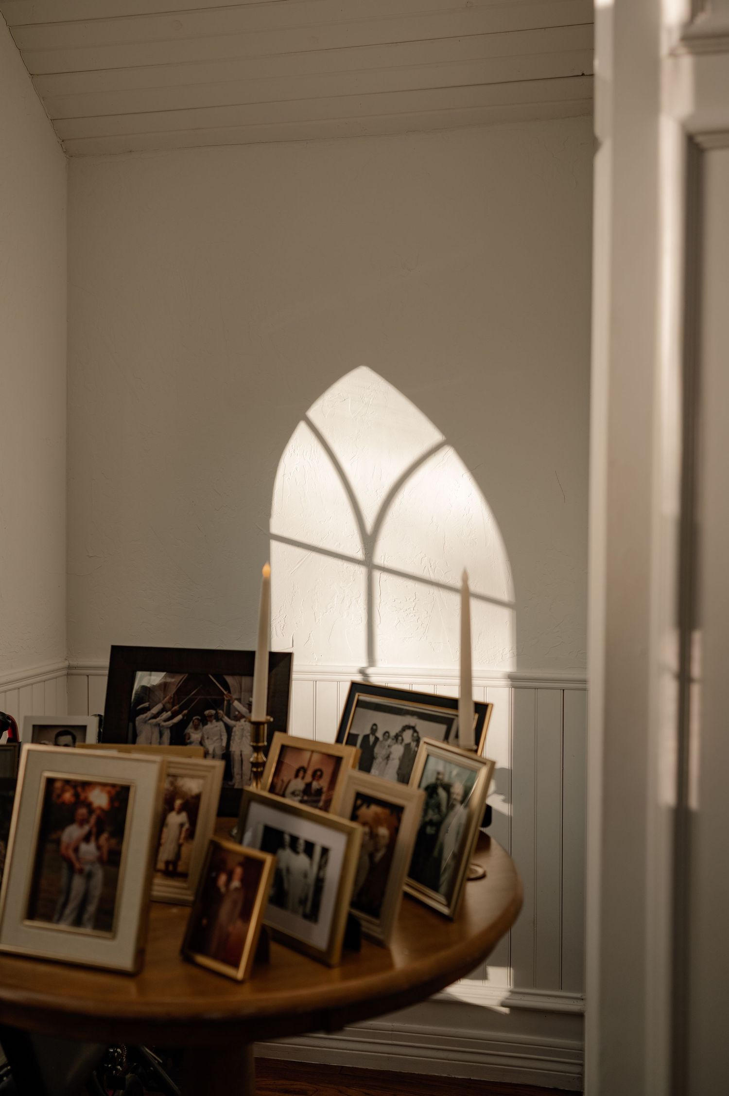 A row of framed photographs displayed at w a wedding ceremony along a wall with arched Gothic-style shadow in the background.