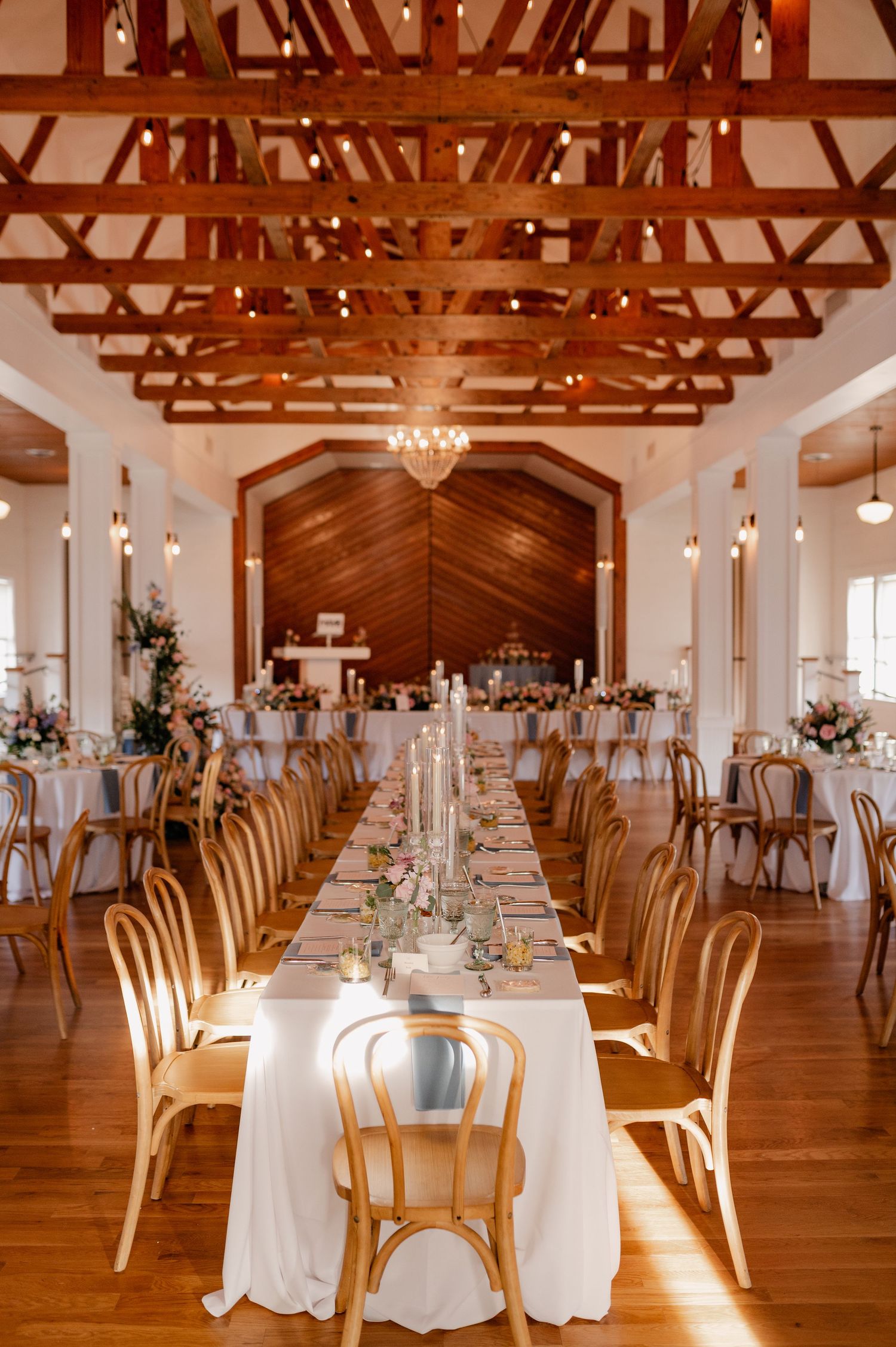 Wedding reception venue in Dallas, Texas with exposed wooden beams, chandelier, and long tables set with white linens.