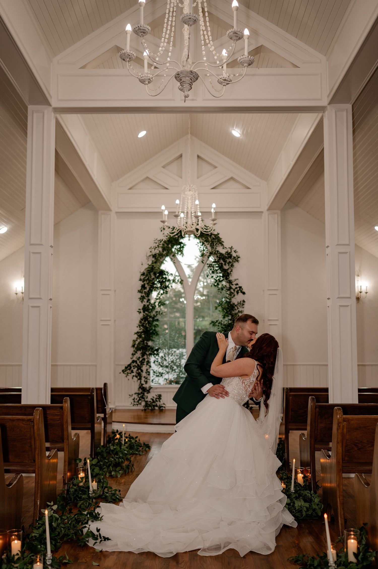 Intimate photo of groom dip kissing his bride down a cozy aisle during wedding couple portraits in a chapel venue in Denton, Texas